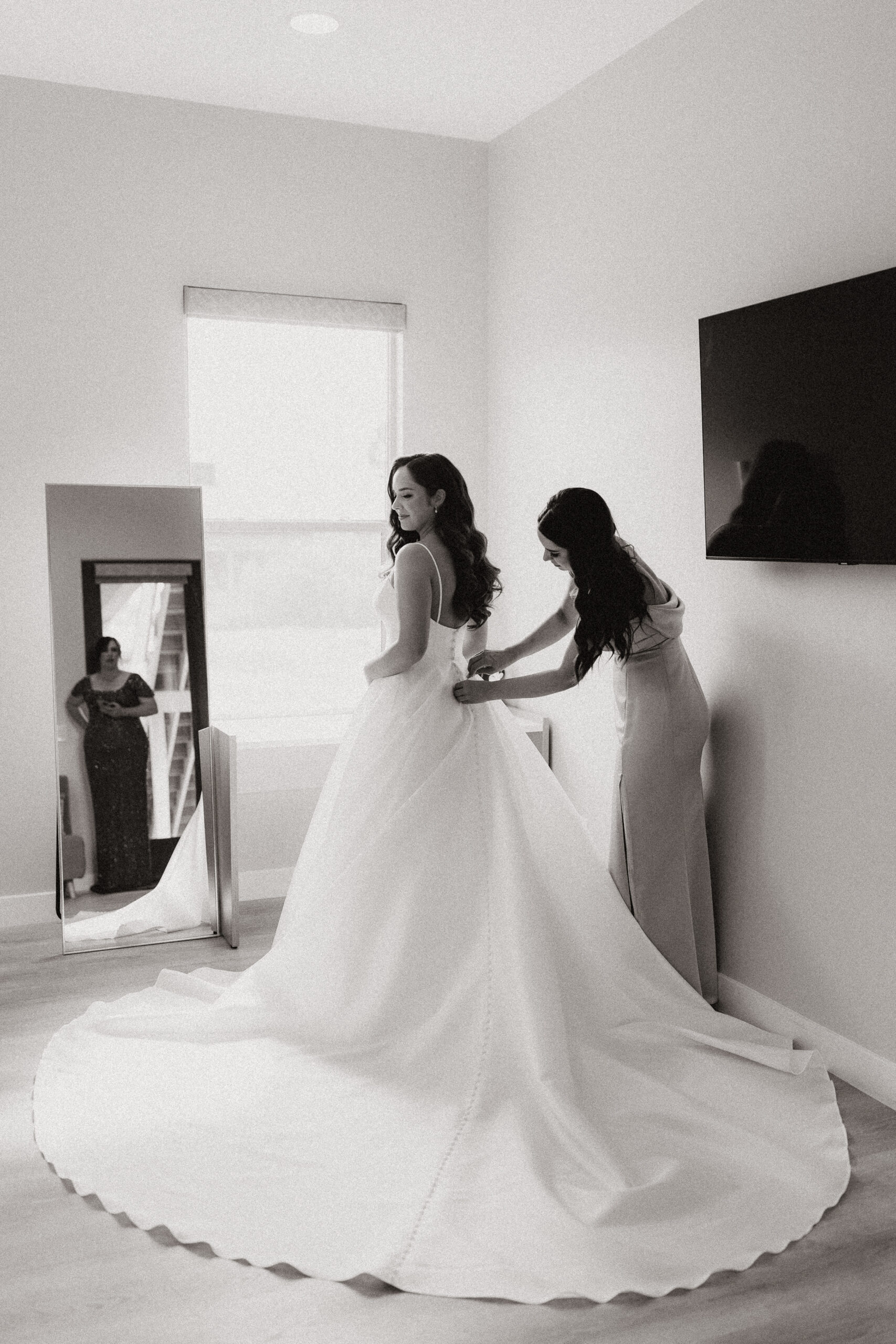 black and white of bride putting dress on with help