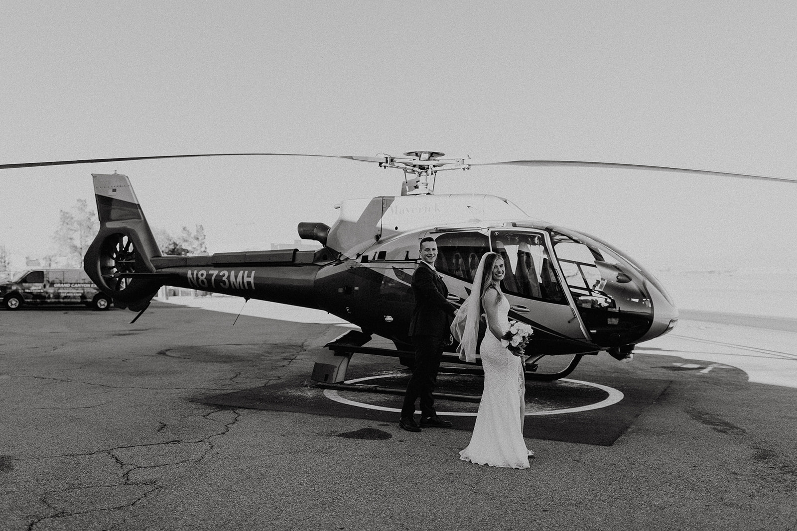 black and white of bride and groom in front of helicopter