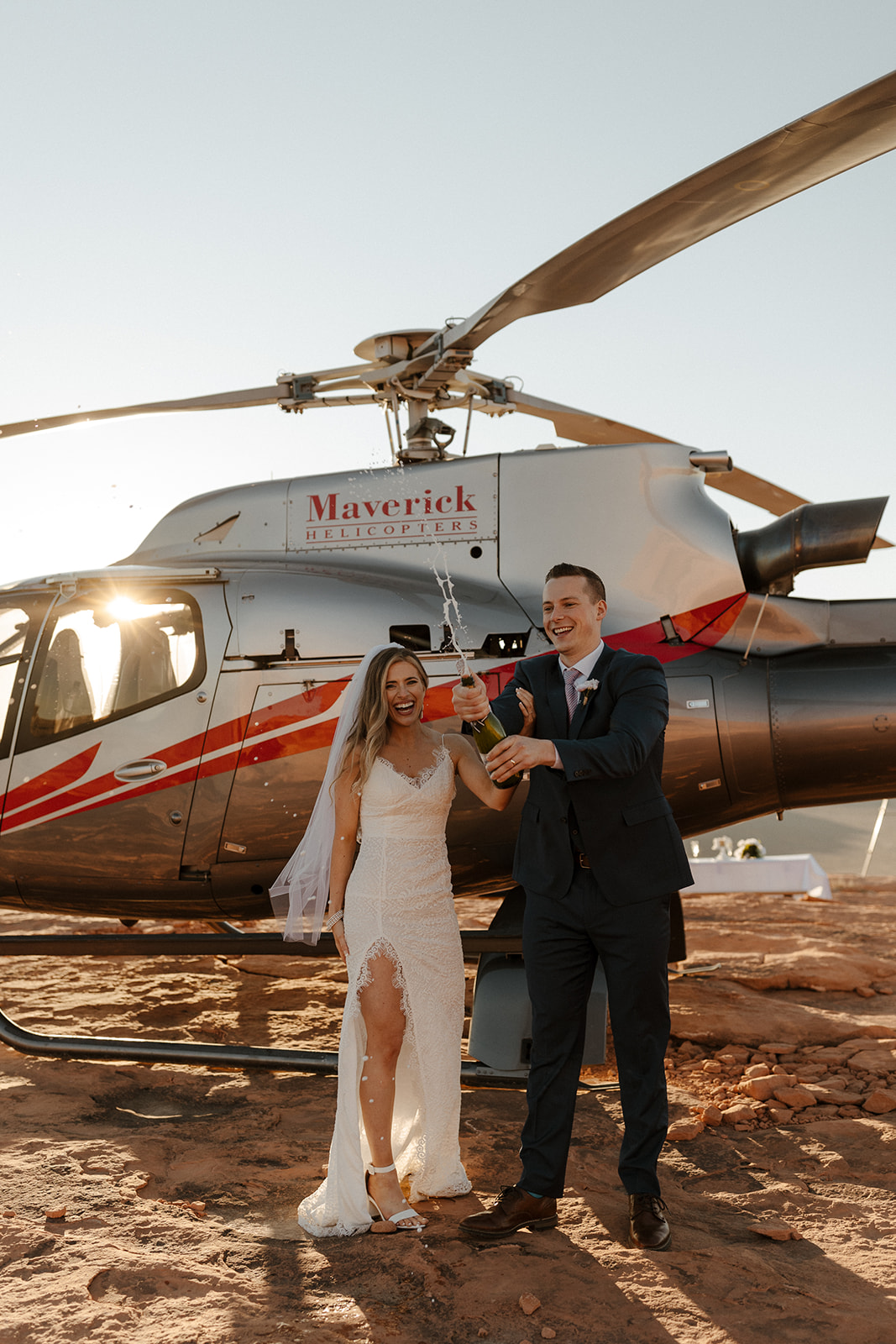 bridal couple popping champagne in front of helicopter
