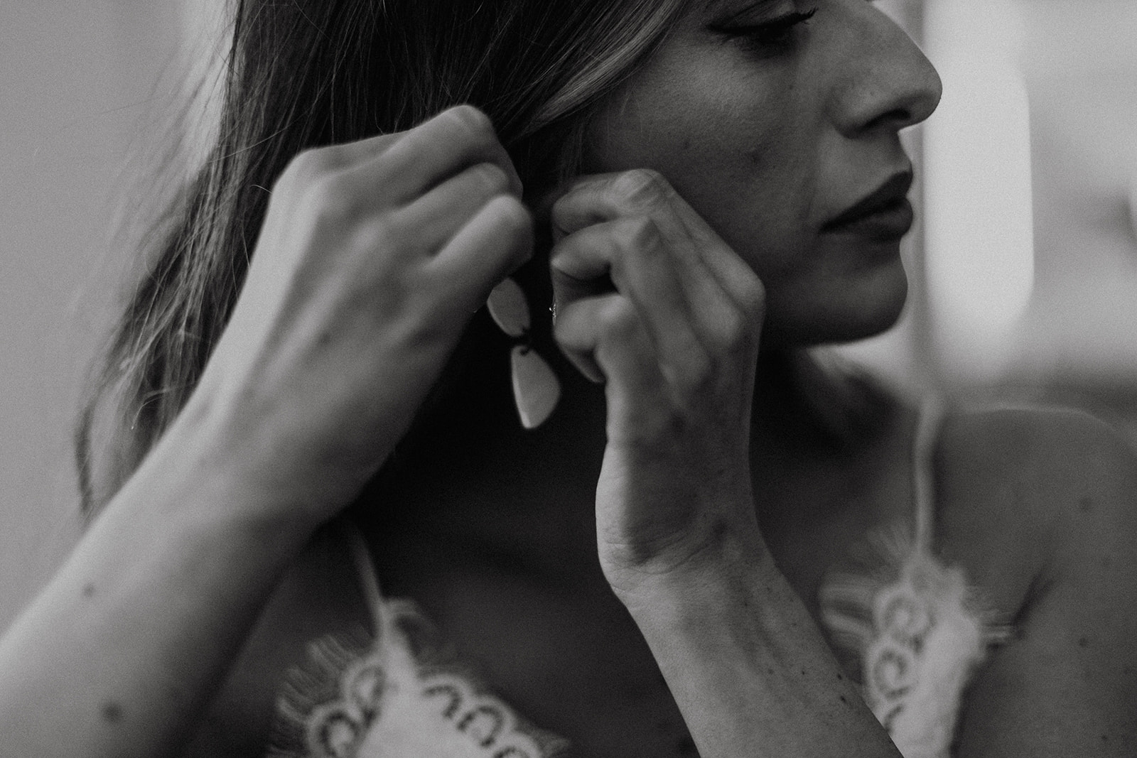 black and white of bride putting on earrings