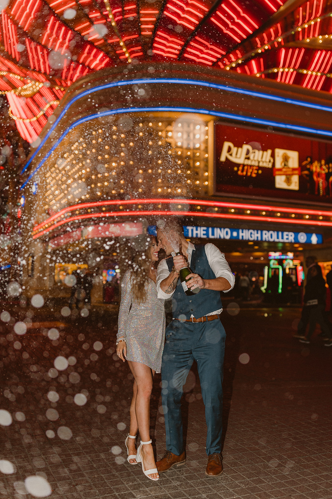 flash photo of bridal couple popping champagne with neon signs in background