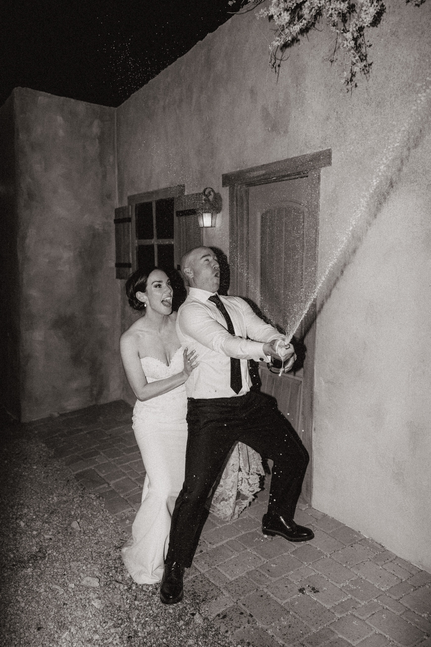 black and white of bride and groom popping champagne