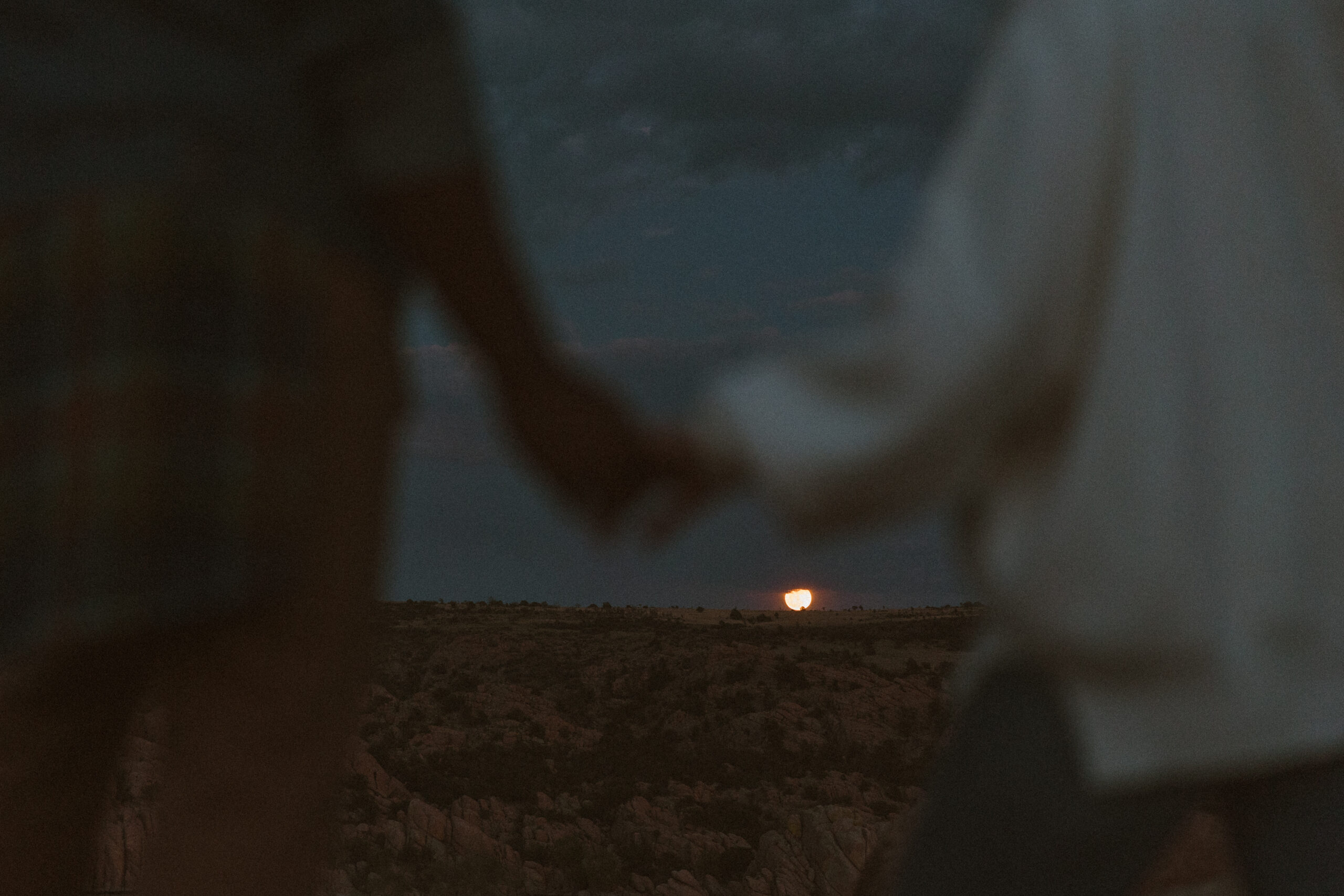 couple holding hands at sunset with the moon rising at watson lake in Arizona 