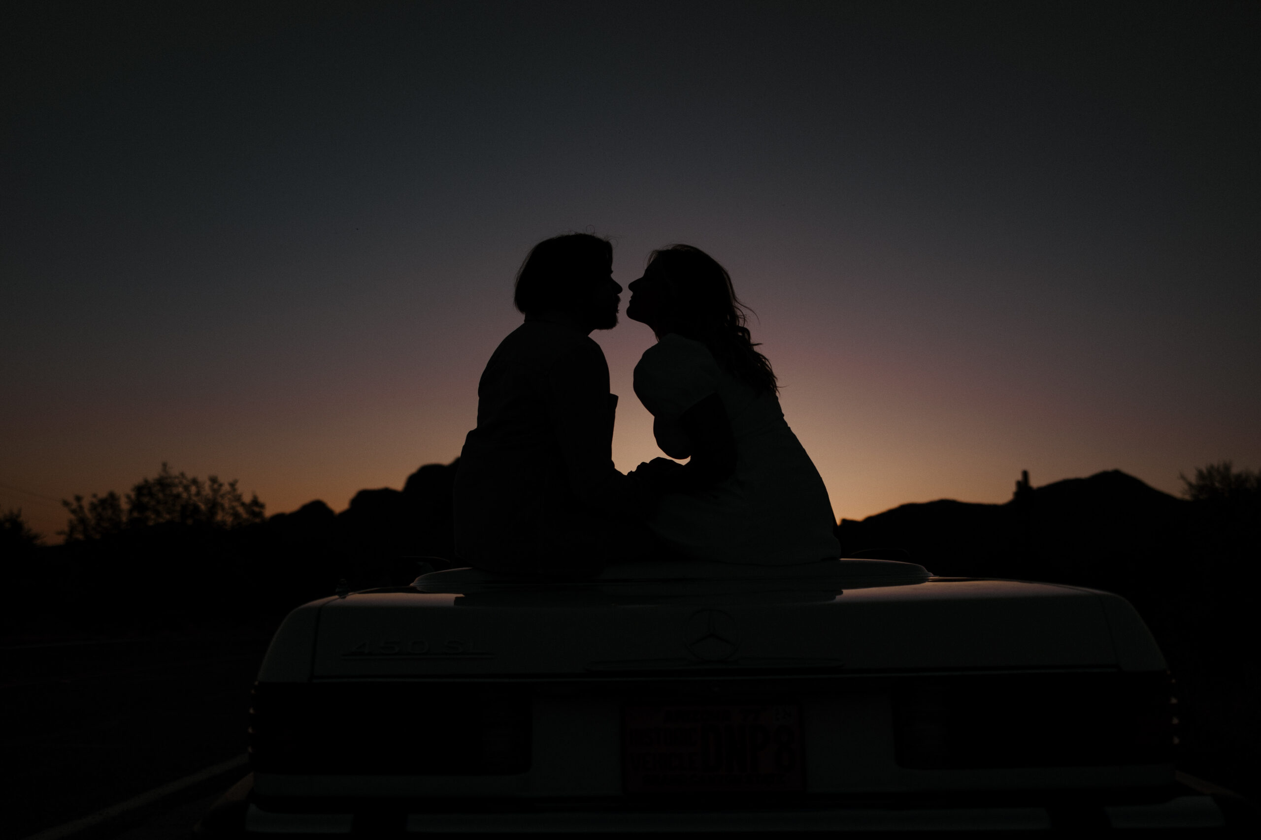 shadow against the sunset of couple sitting on the hood 