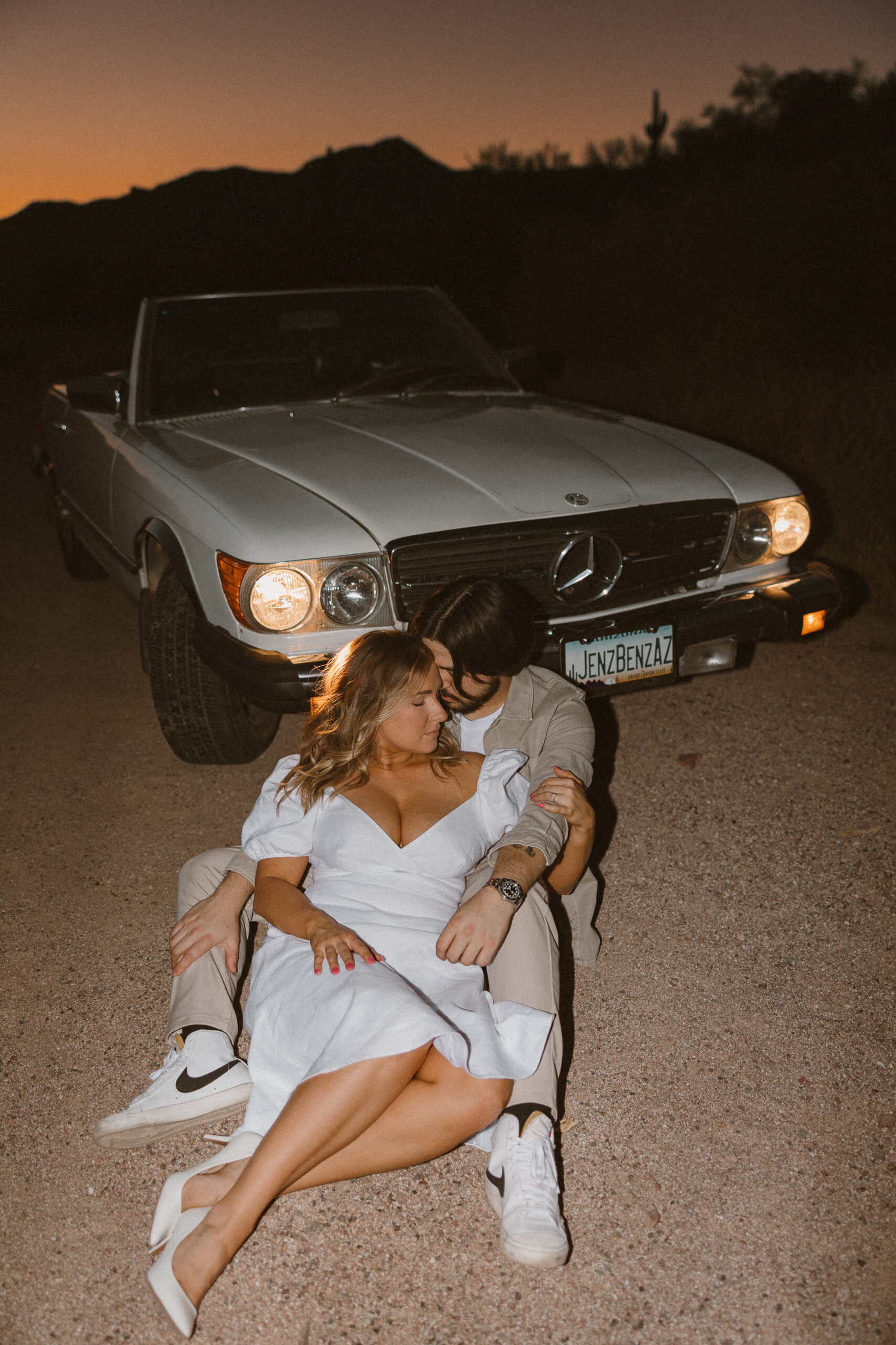 couple holding each other on the ground in front of the car at sunset for vintage car engagement photos