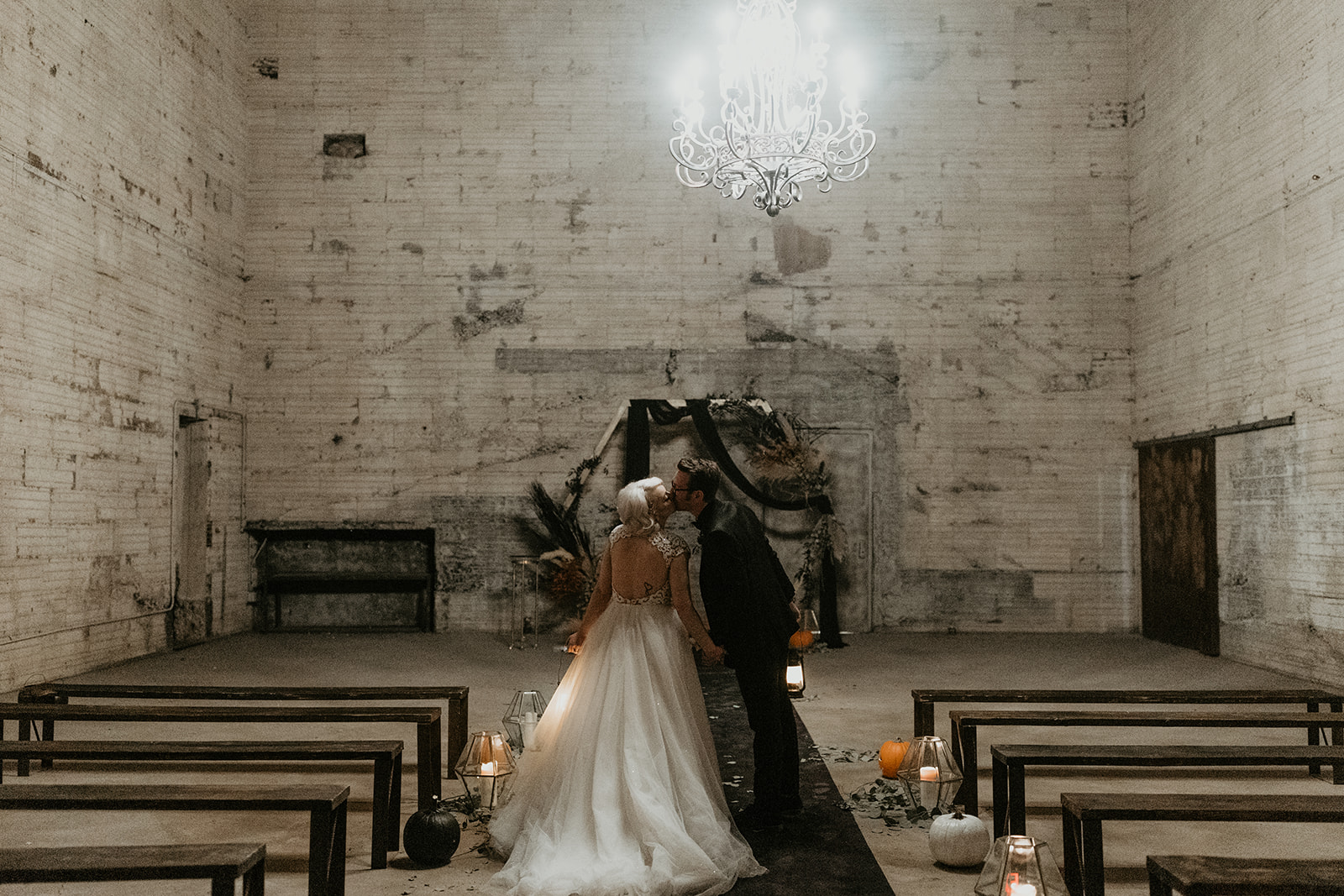 bridal couple in moody ceremony aisle kissing at fall halloween wedding 