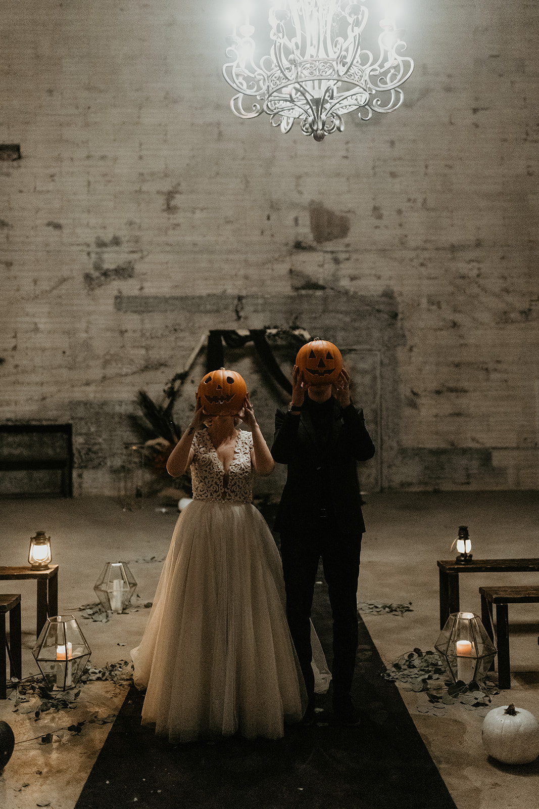 bridal couple standing in ceremony aisle holding up carved pumpkins in front of their face