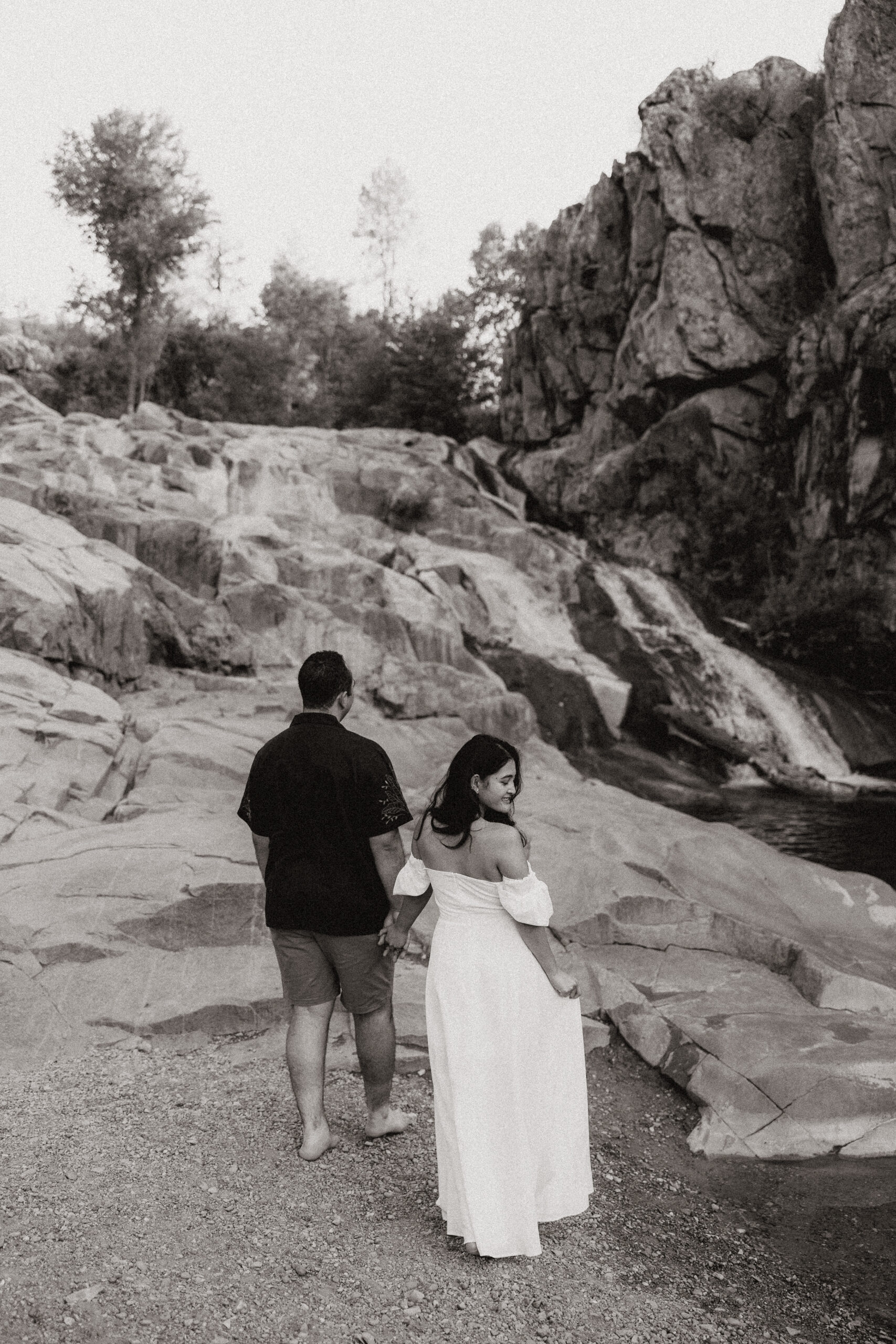 black and white of engaged couple walking towards waterfall at engagement photos