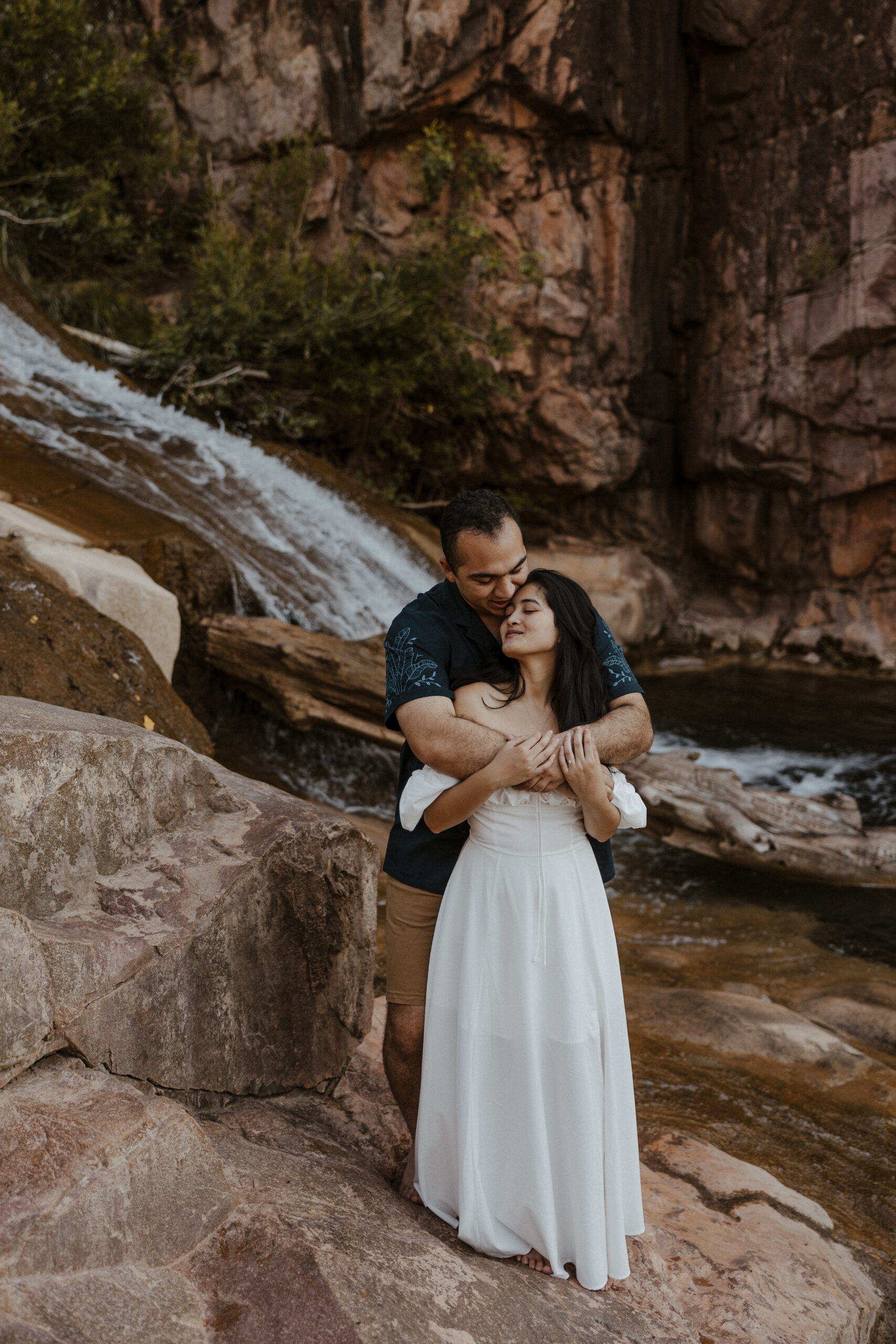 engaged couple standing in front of waterfall at engagement photos holding each other