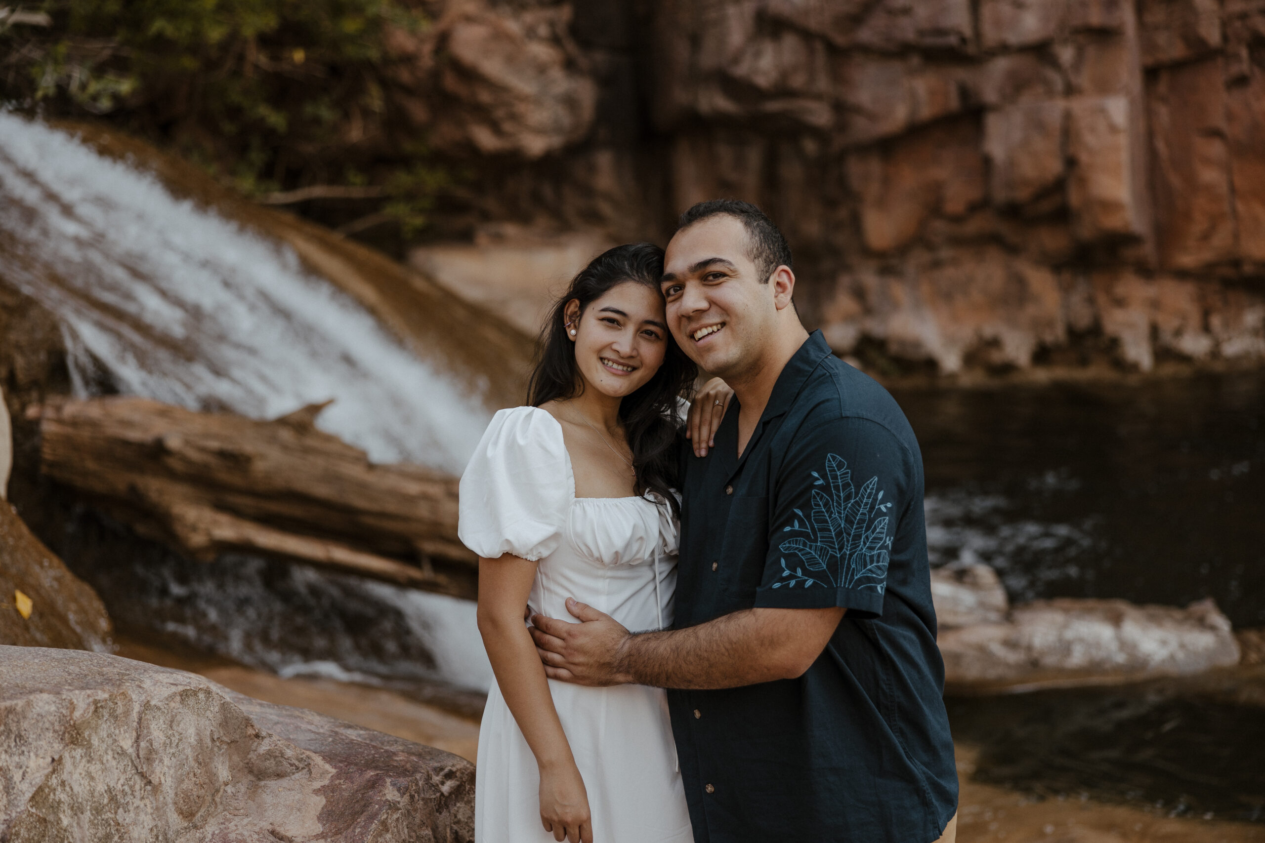 engaged couple smiling in front of waterfall at engagement photos
