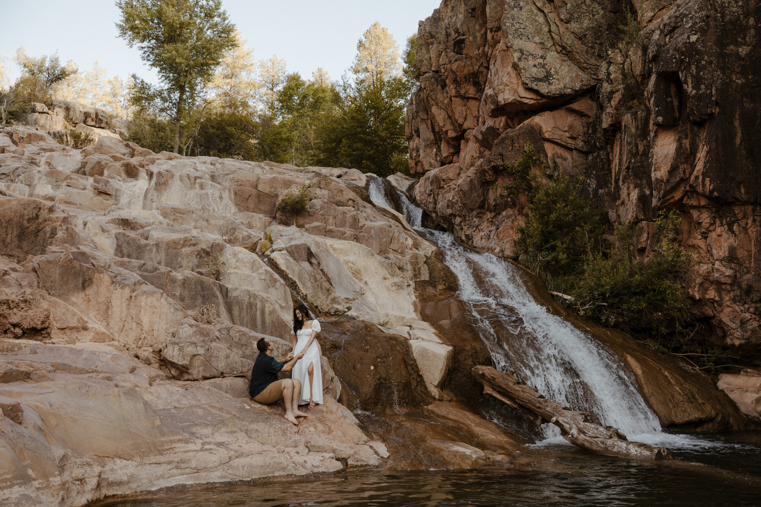 zoomed out engaged couple standing by waterfall at engagement photos