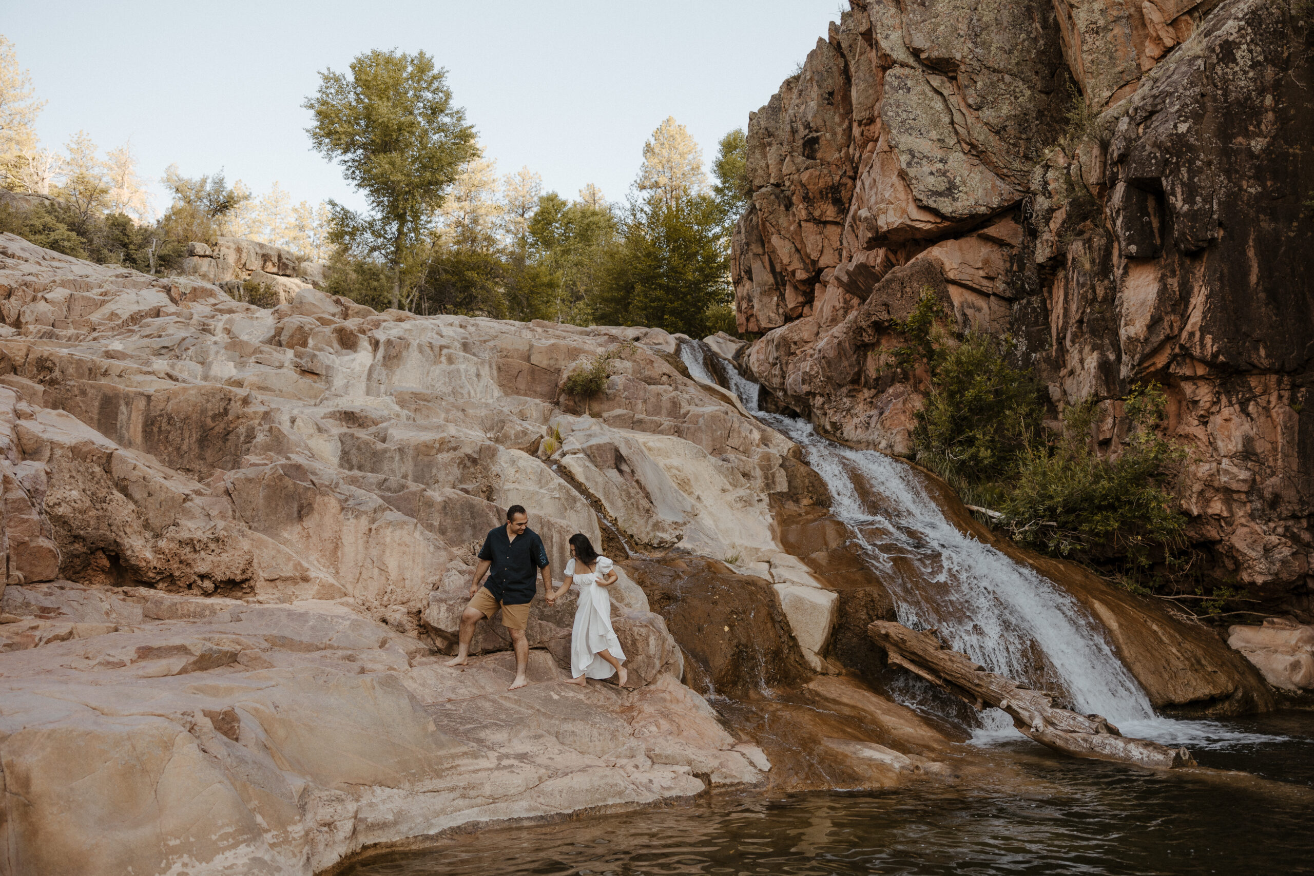 zoomed out engaged couple standing by waterfall at engagement photos