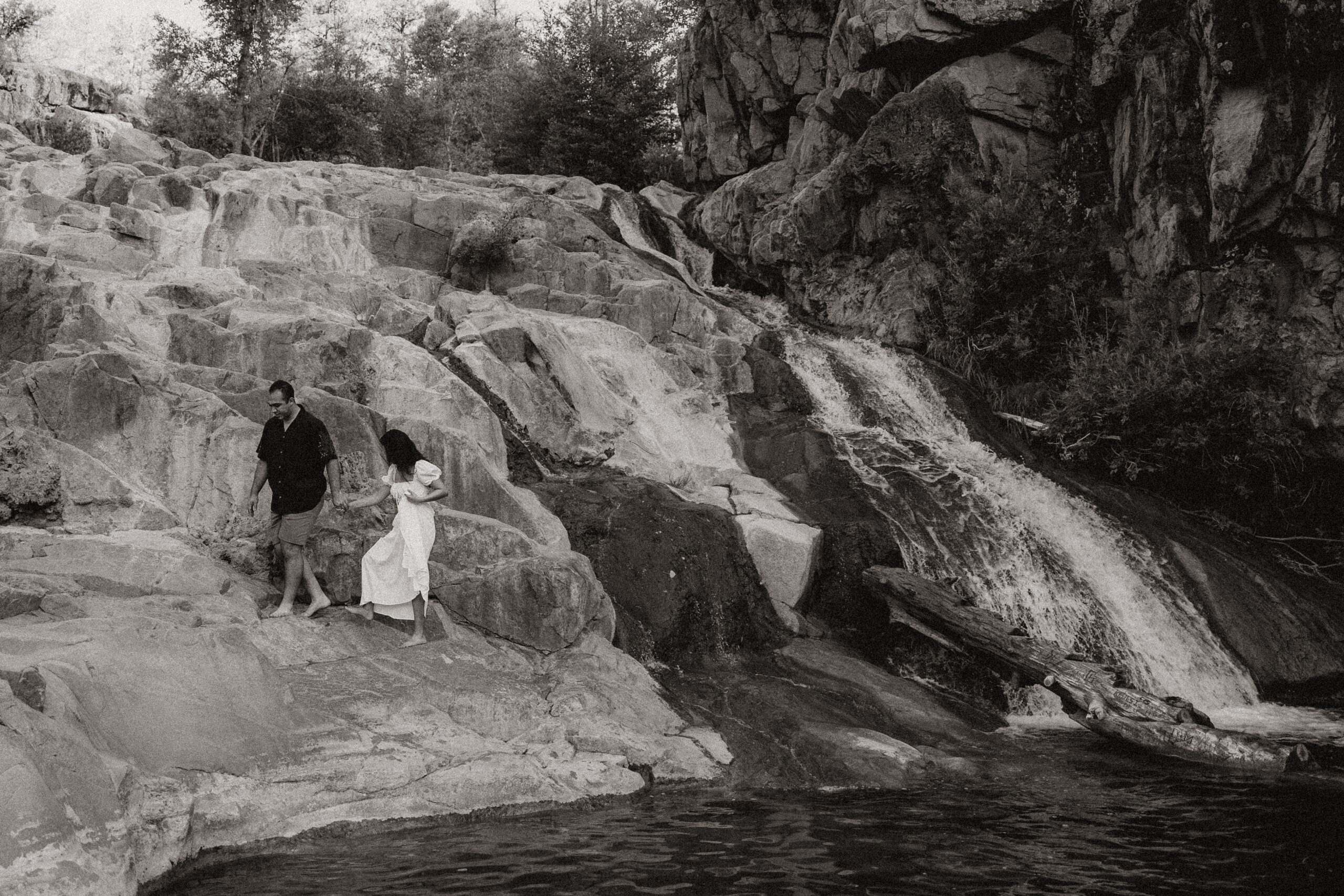 black and white of engaged couple standing by waterfall at engagement photos