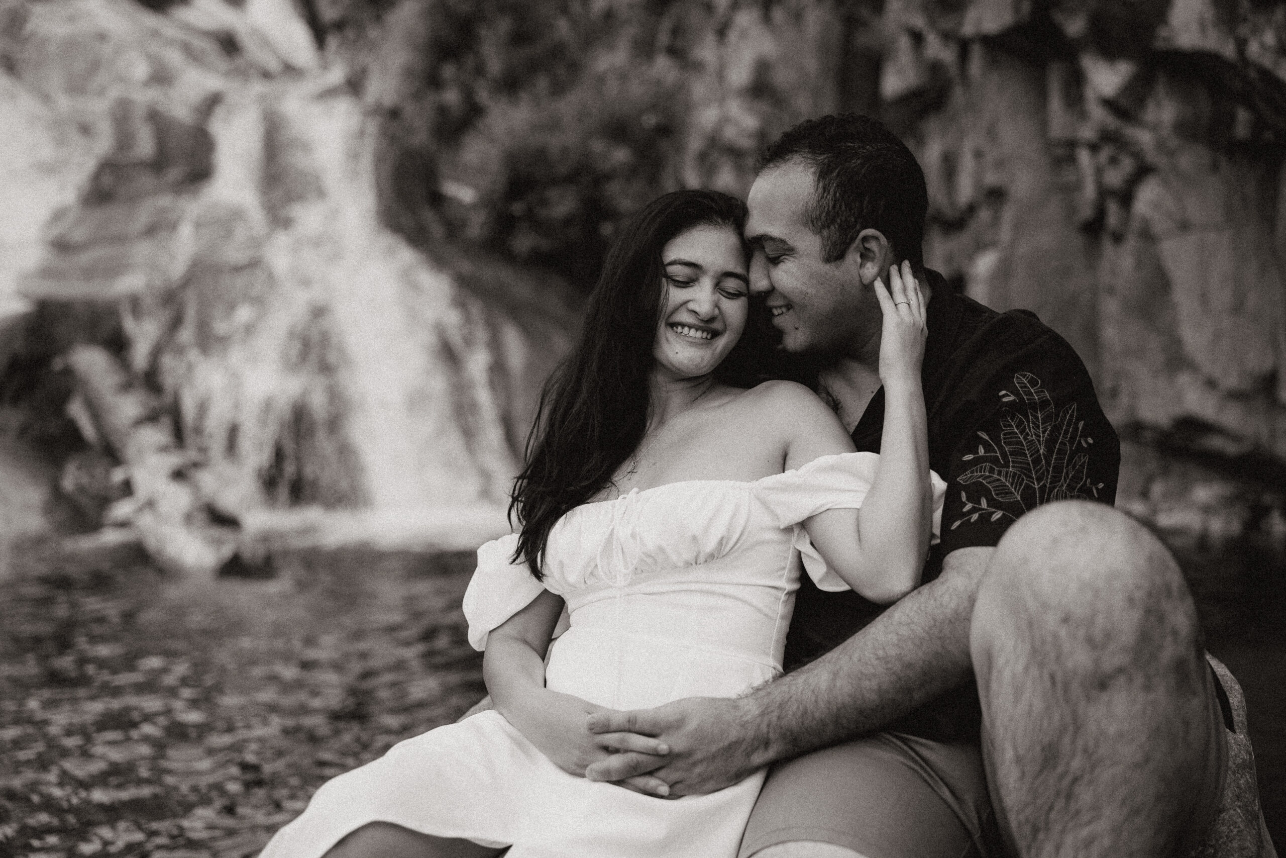 black and white of engaged couple sitting on a rock by waterfall at engagement photos