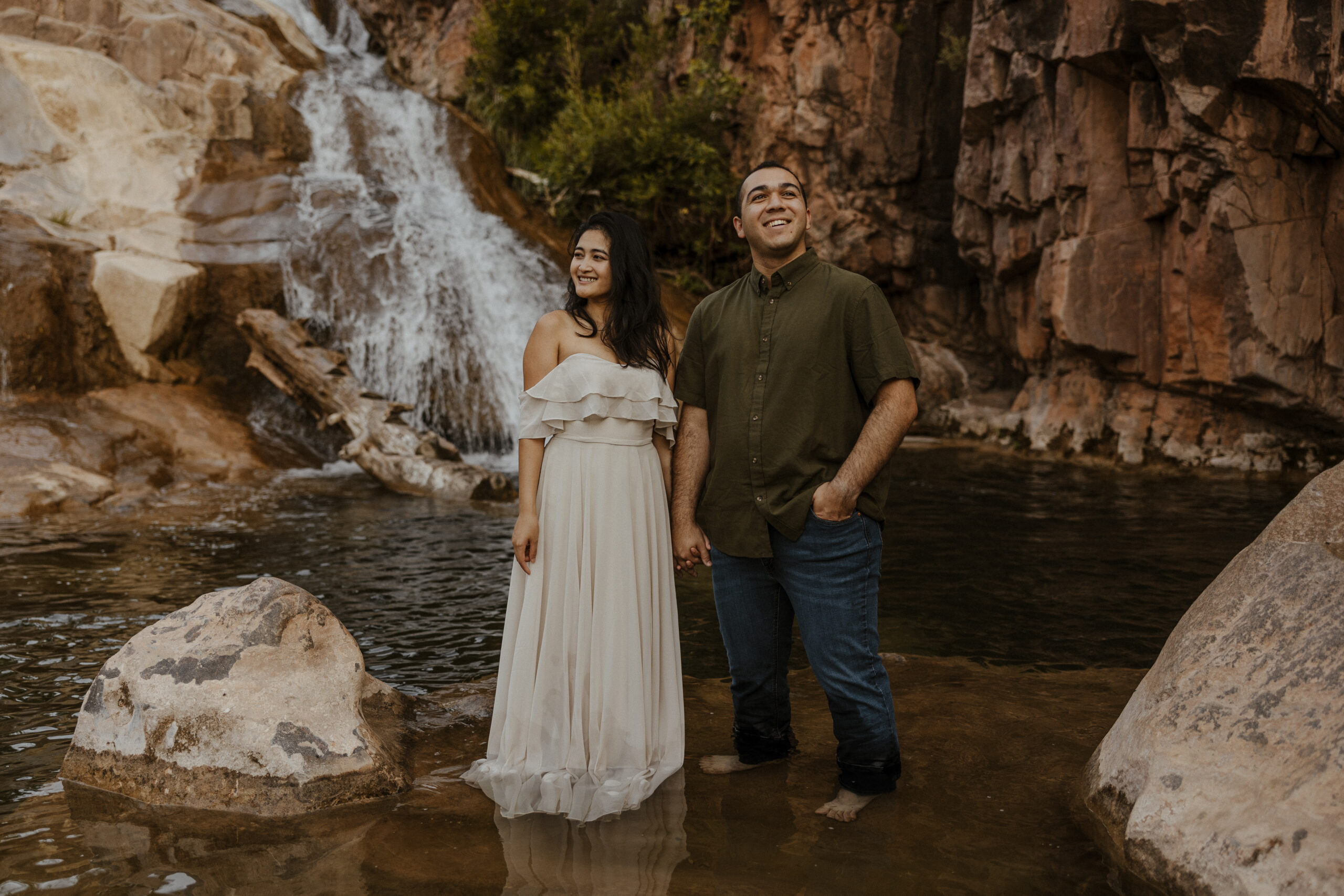 engaged couple standing in front of waterfall looking in opposite directions