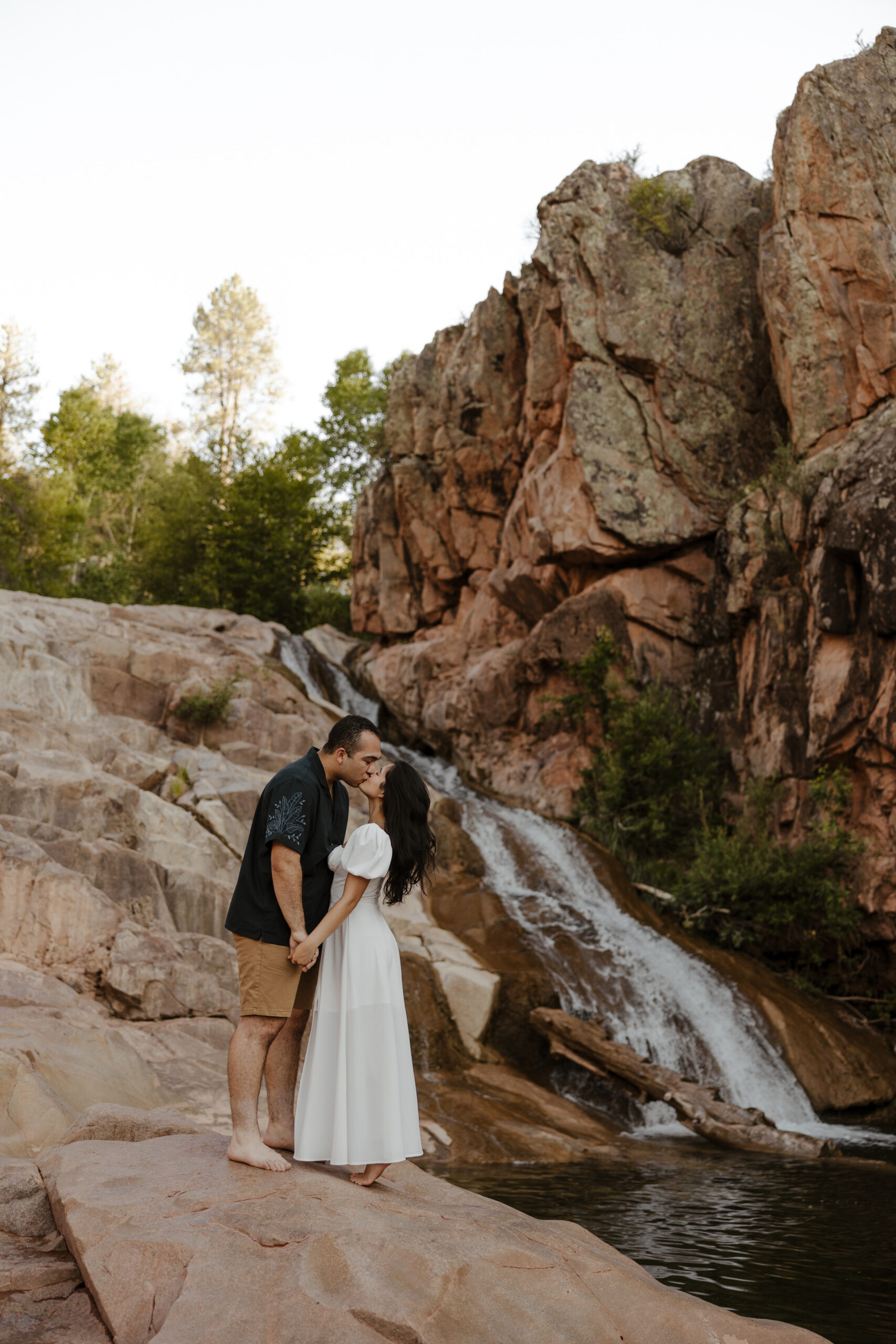 engaged couple kissing and holding hands in front waterfall at engagement photos