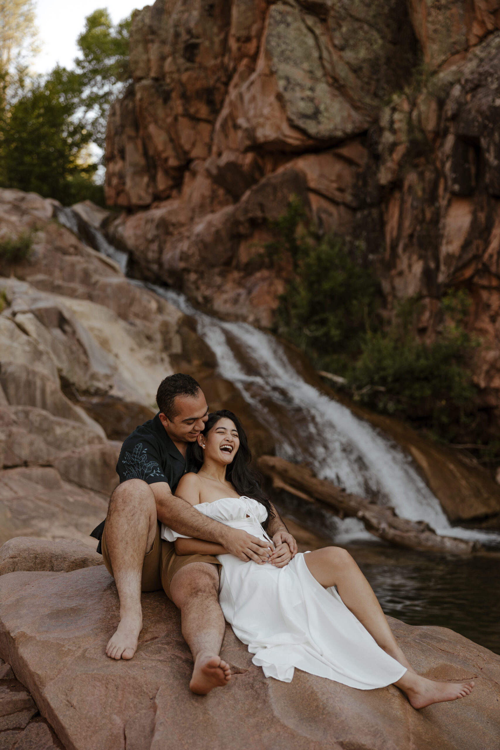 engaged couple sitting and laughing in front waterfall at engagement photos