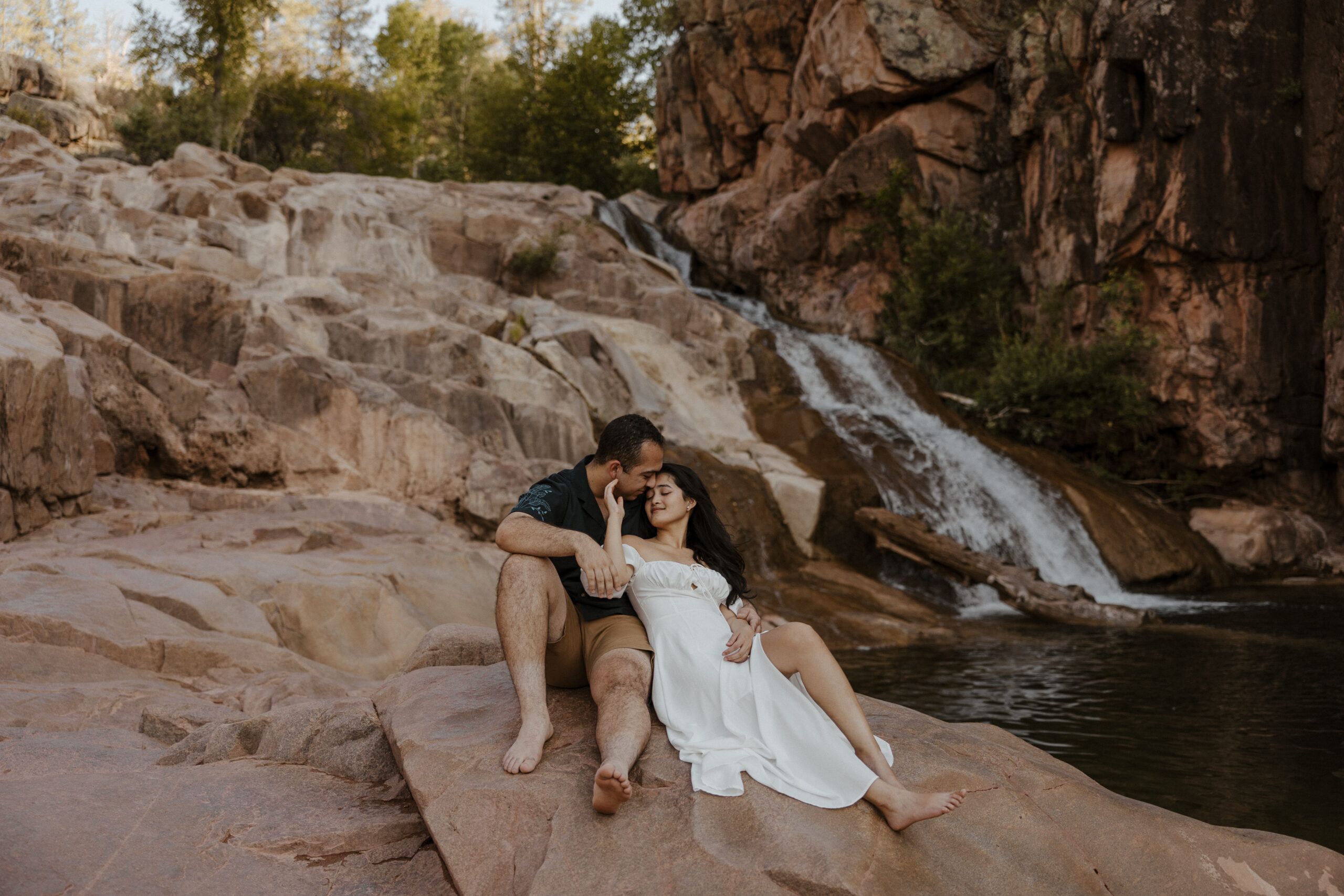 engaged couple sitting on rocks at waterfall engagement photos