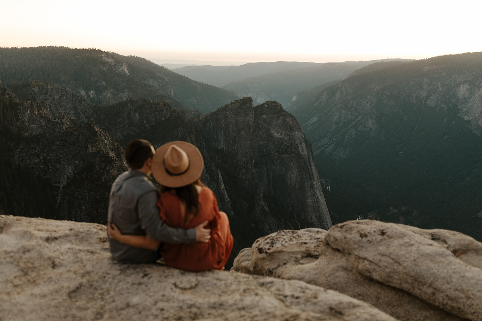couple sitting and holding each other on taft point in yosemite park