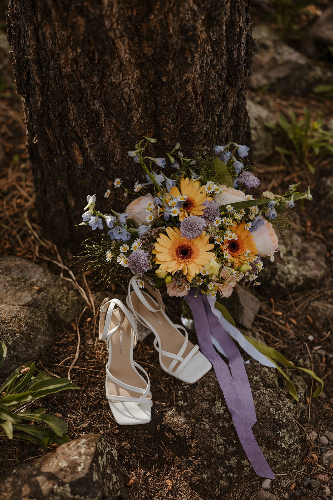 bride's bouquet and shows by a tree at intimate forest wedding 
