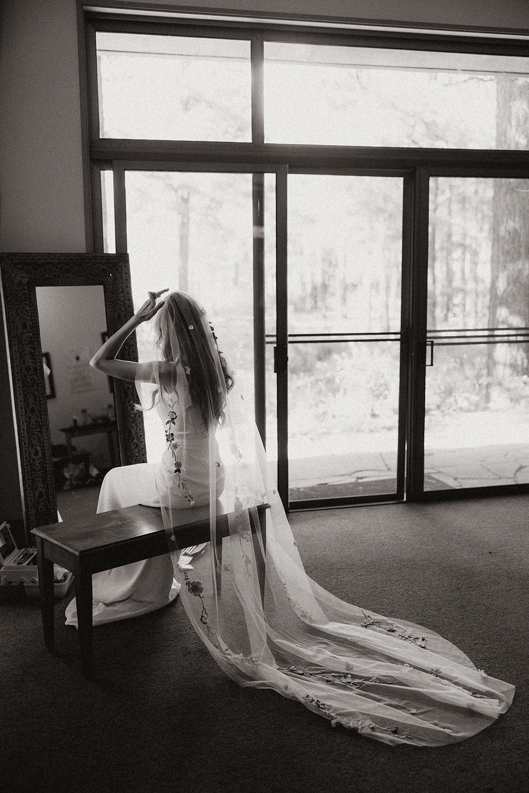 bride sitting and adjusting her floral embroidered veil at intimate forest wedding 