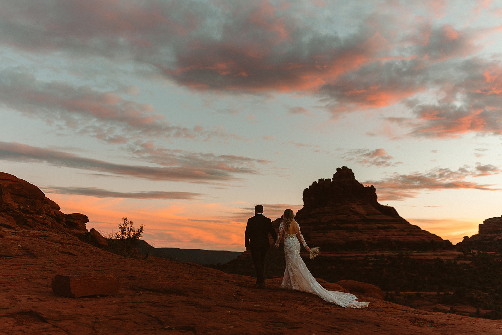 bridal couple walking on rocks at sunset 