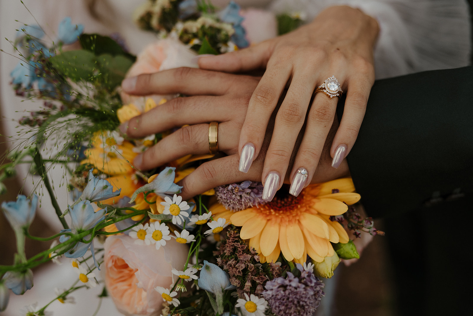 bridal couple's hands with wedding rings resting on bright flowers