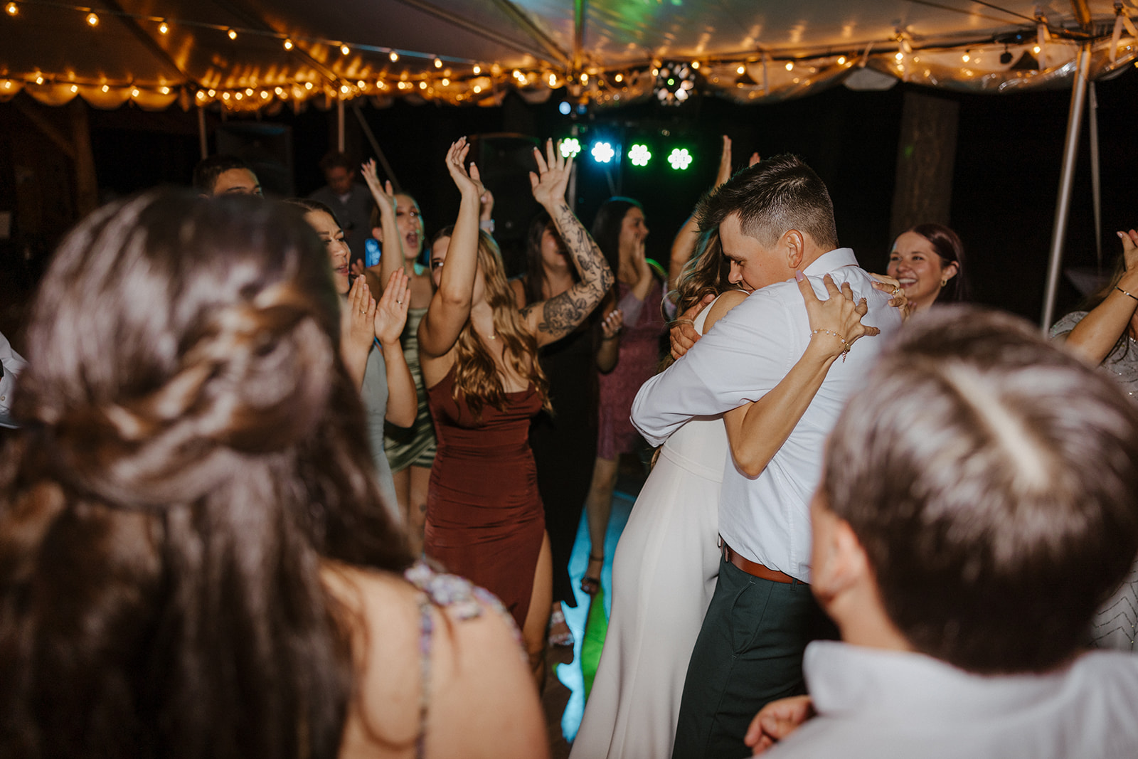 bride and groom hugging while dancing in the middle of wedding guests 