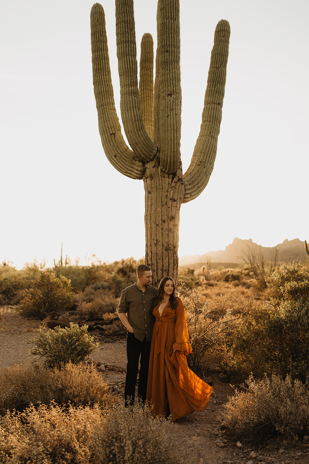 couple standing in front of a giant cactus at sunrise at lost dutchman state park in az