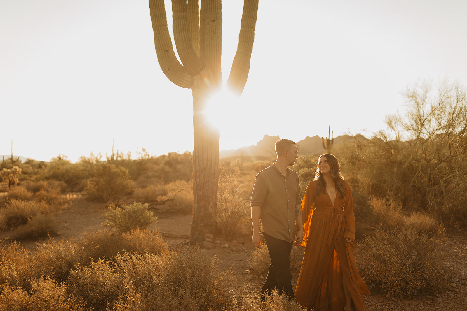 engaged couple walking with the sunrise shining through the cactus