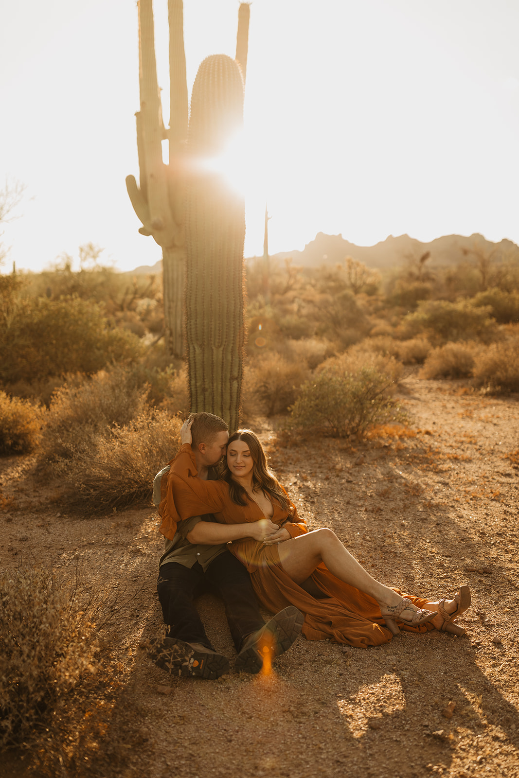 couple sitting in front of a giant cactus at sunrise at lost dutchman state park in az