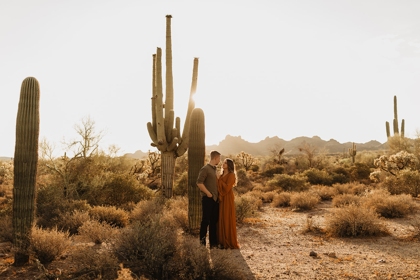 couple embracing with cacti and desert landscape background during sunrise session at lost dutchman state park in az