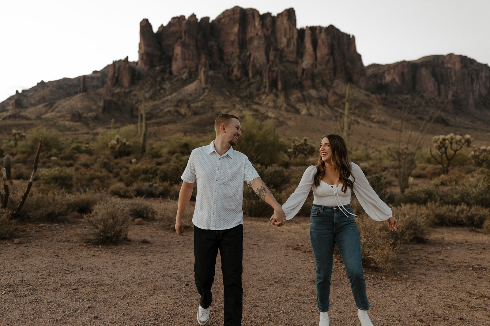 engaged couple holding hands, smiling and walking at lost dutchman state park az engagement session
