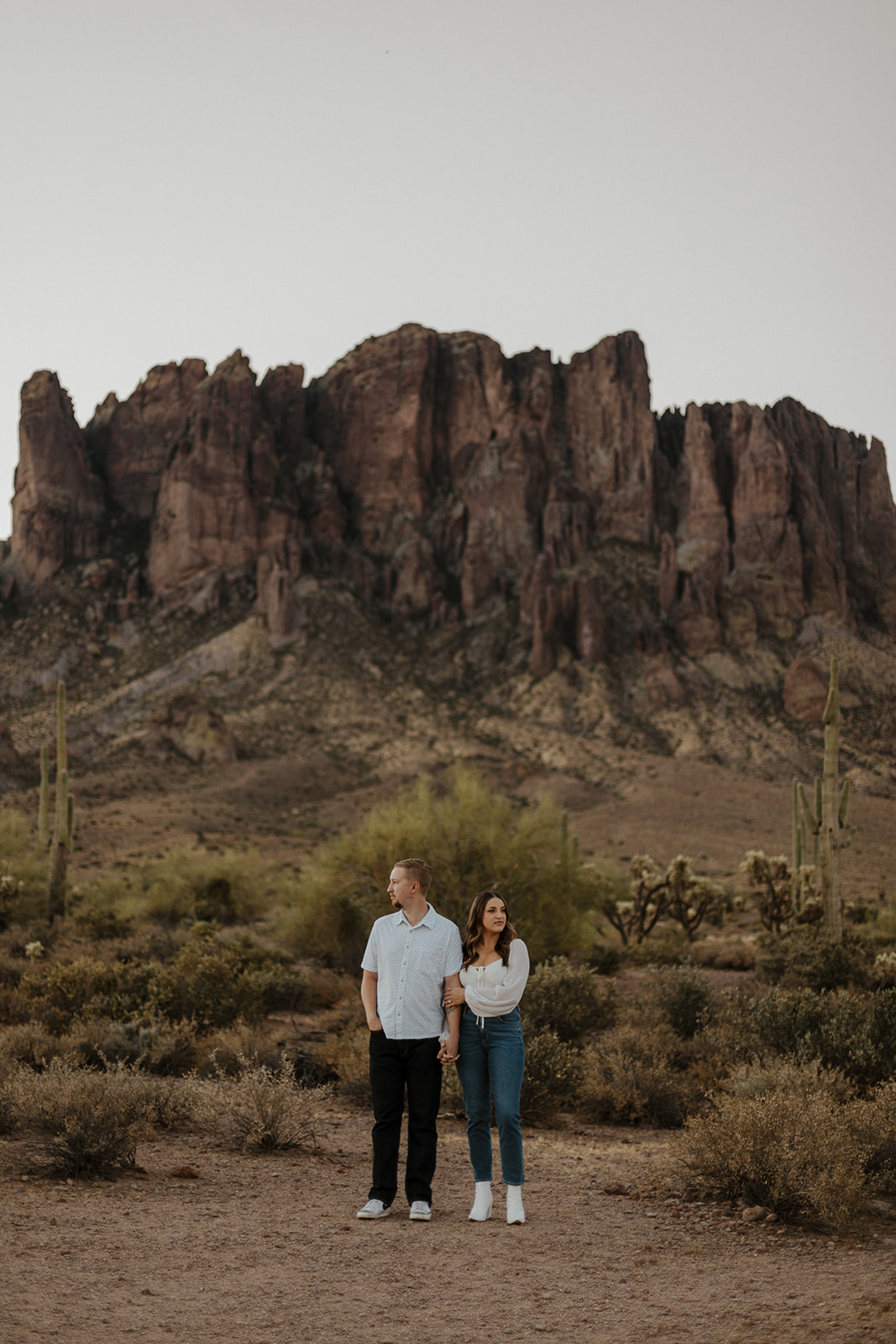 engaged couple holding hands looking in opposite directions at lost dutchman state park az engagement session