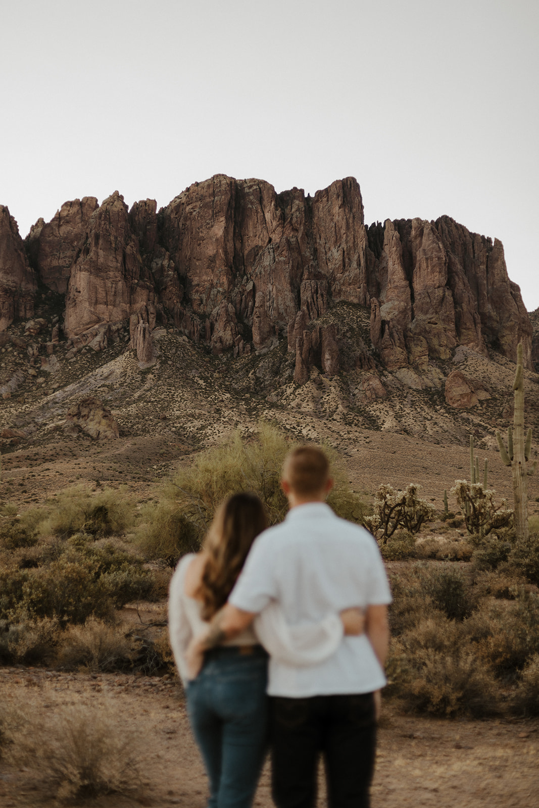 couple blurred out with cacti and desert landscape background in focus during sunrise session at lost dutchman state park in az
