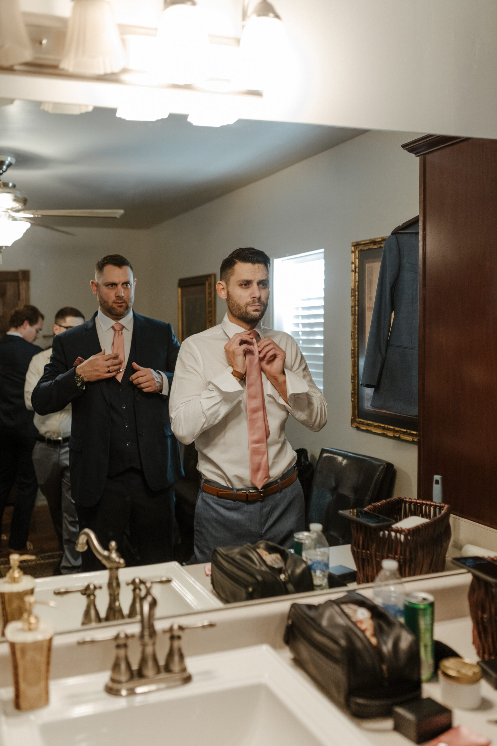 groom looking into the mirror while putting on his tie 
