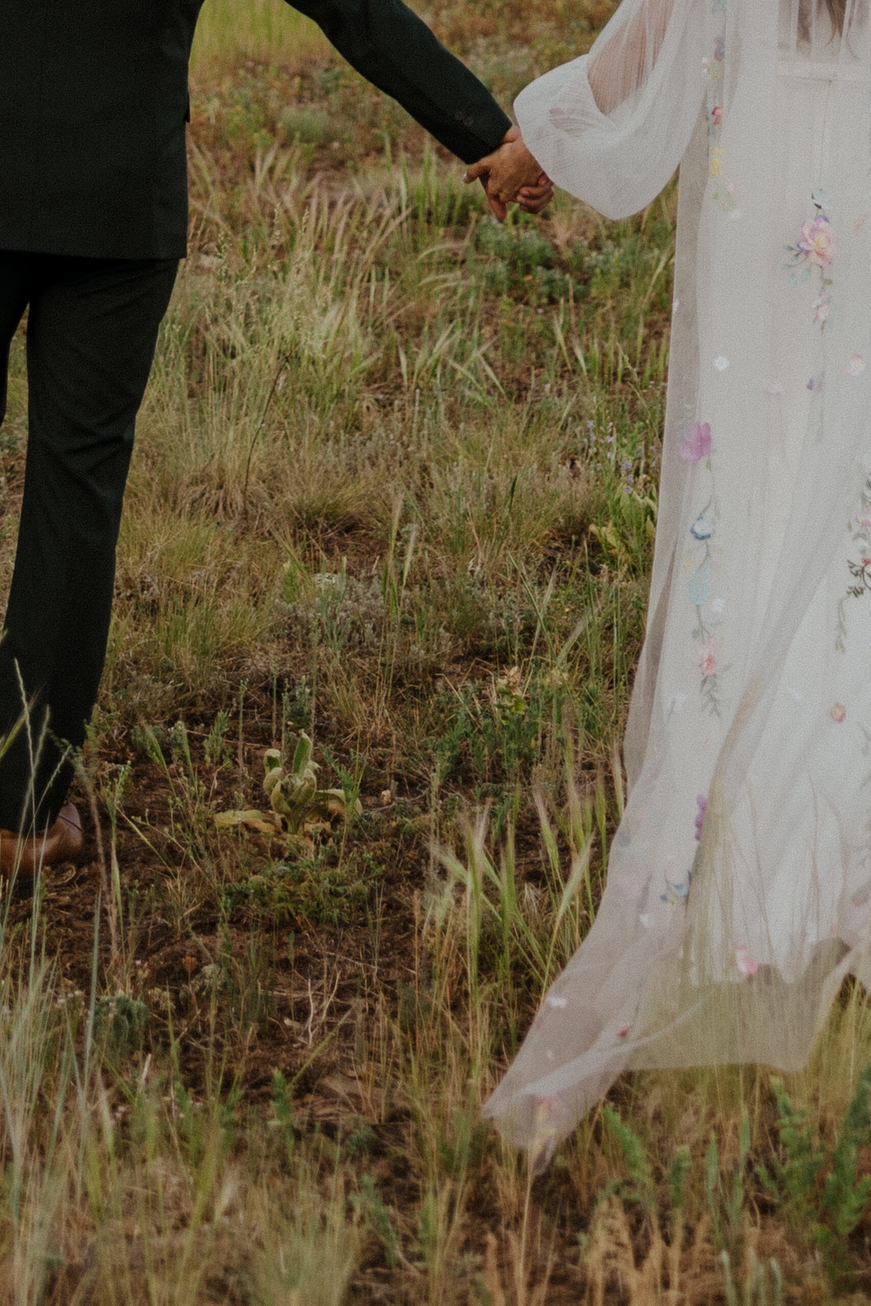 detail shot of grass and bridal couple holding hands at intimate forest wedding 