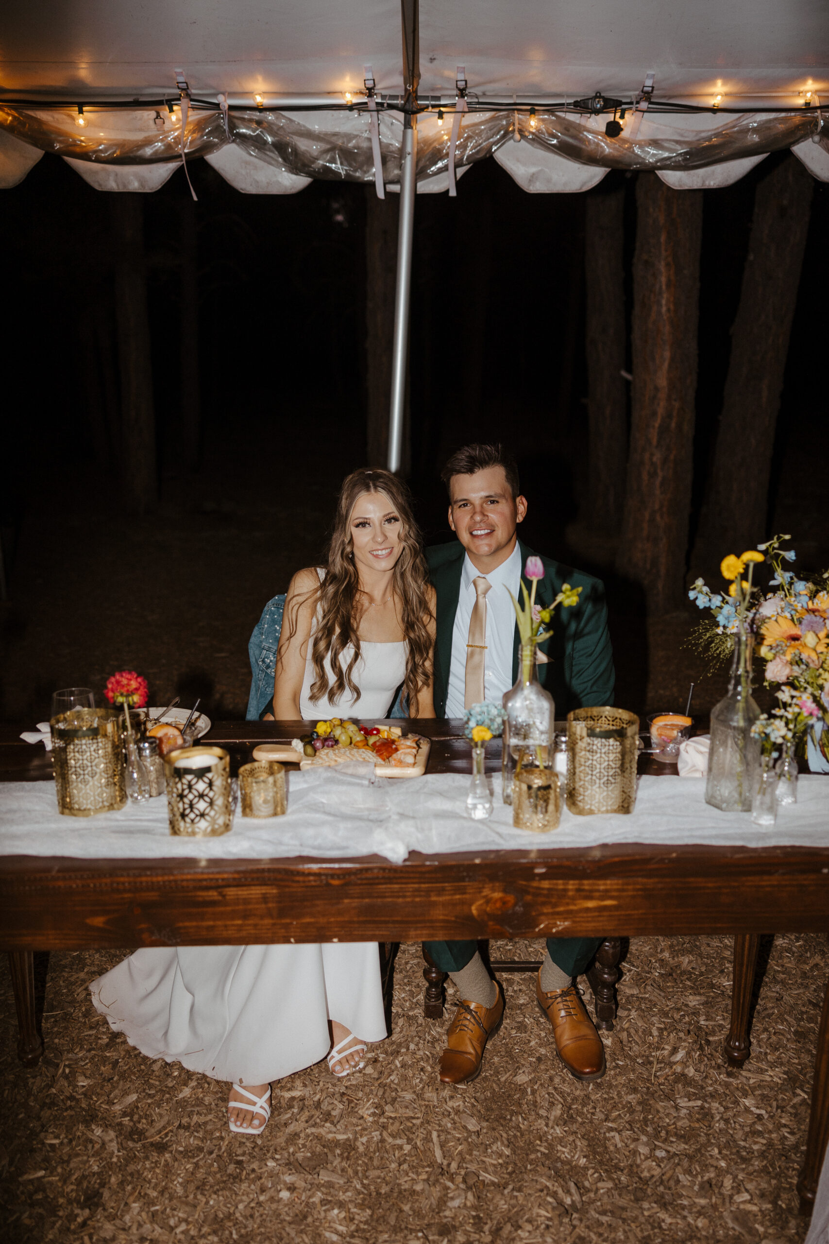 bride and groom smiling at reception head table at intimate forest wedding 