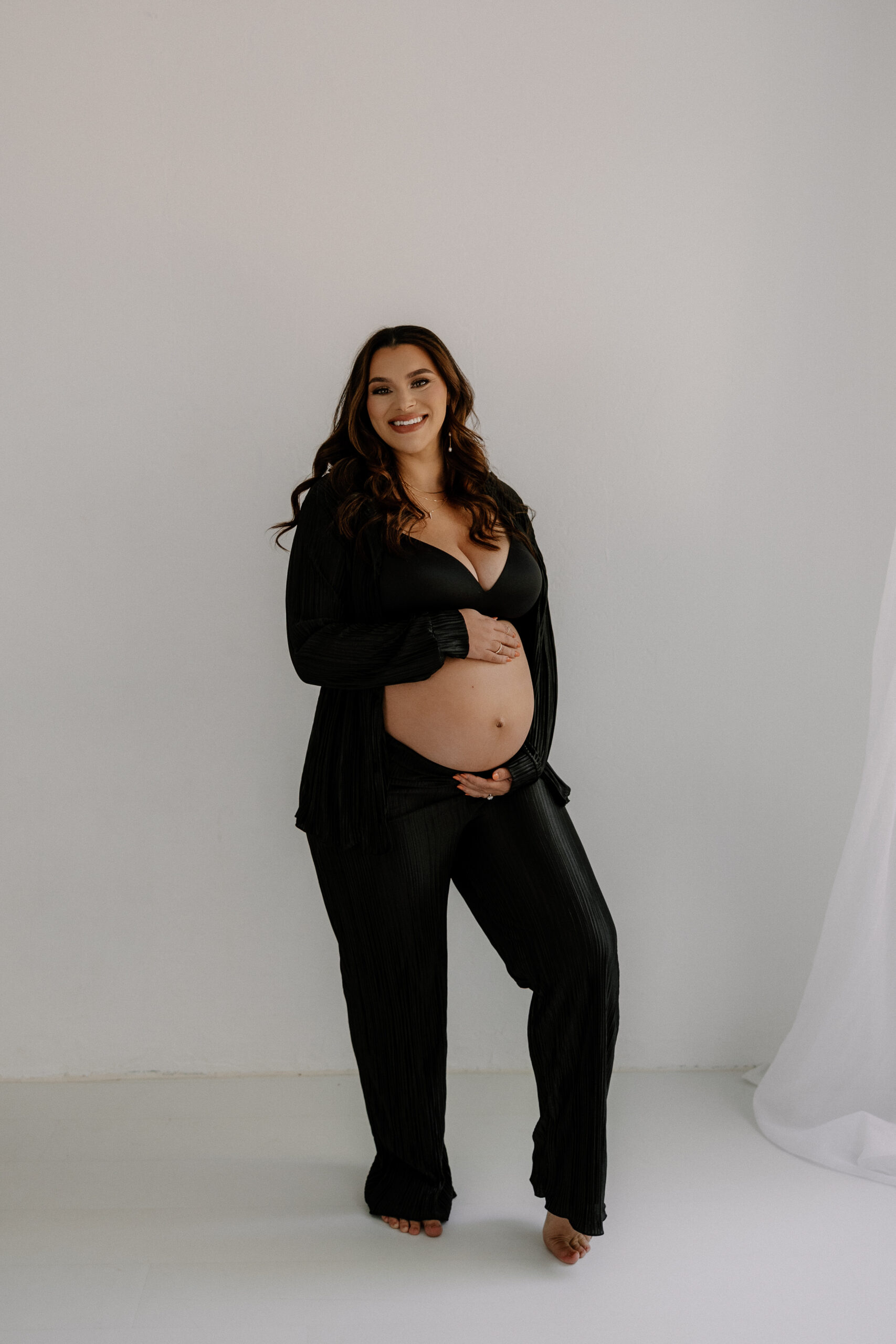mom to be standing, holding stomach and smiling during editorial maternity photoshoot