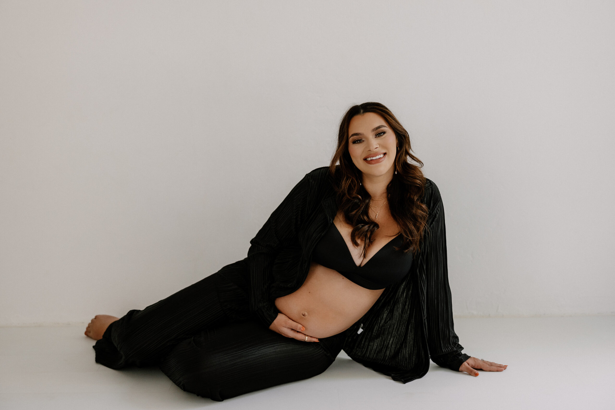 mom to be sitting on the floor smiling at the camera during editorial maternity photoshoot