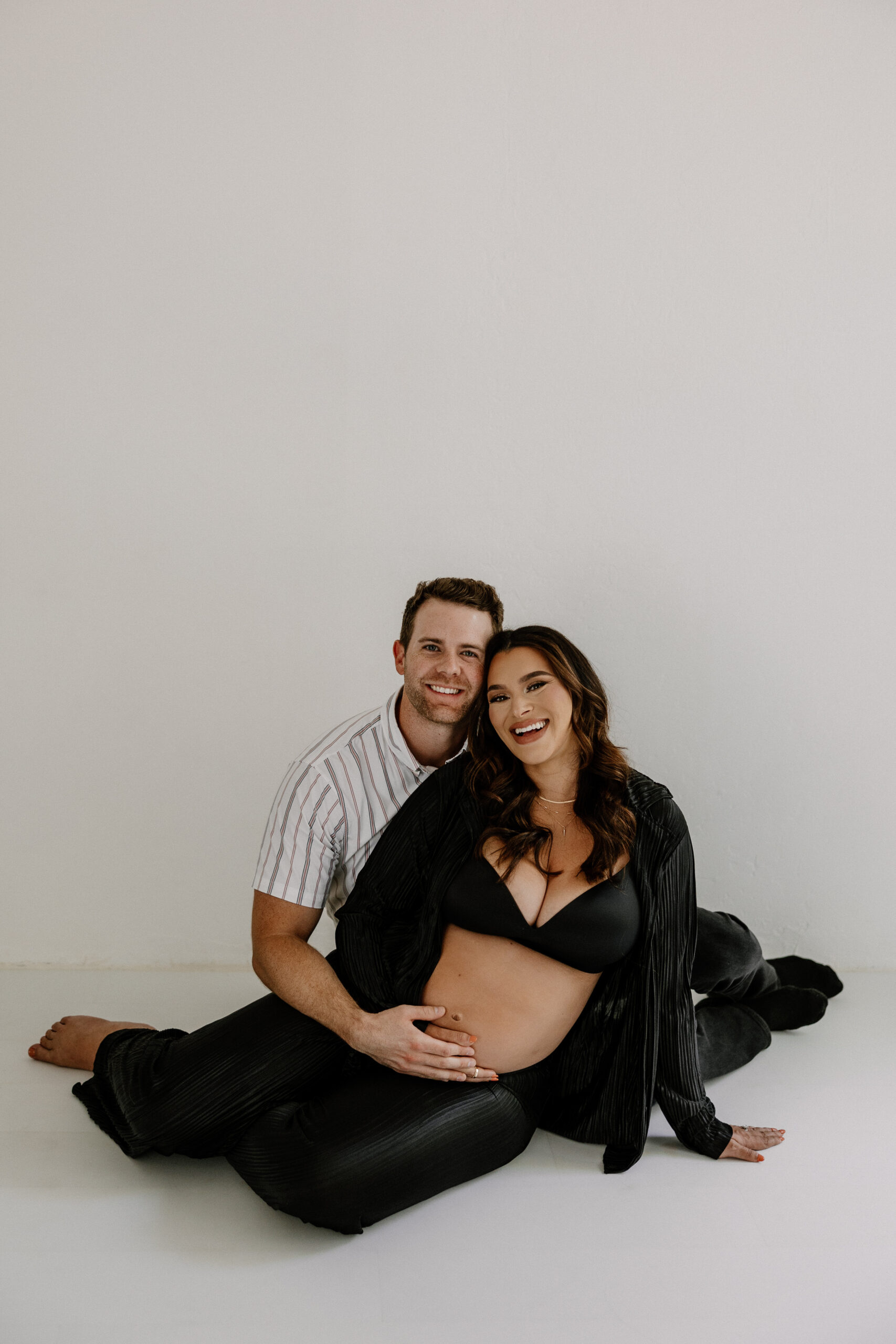 couple smiling and sitting on the floor together during their editorial maternity photos