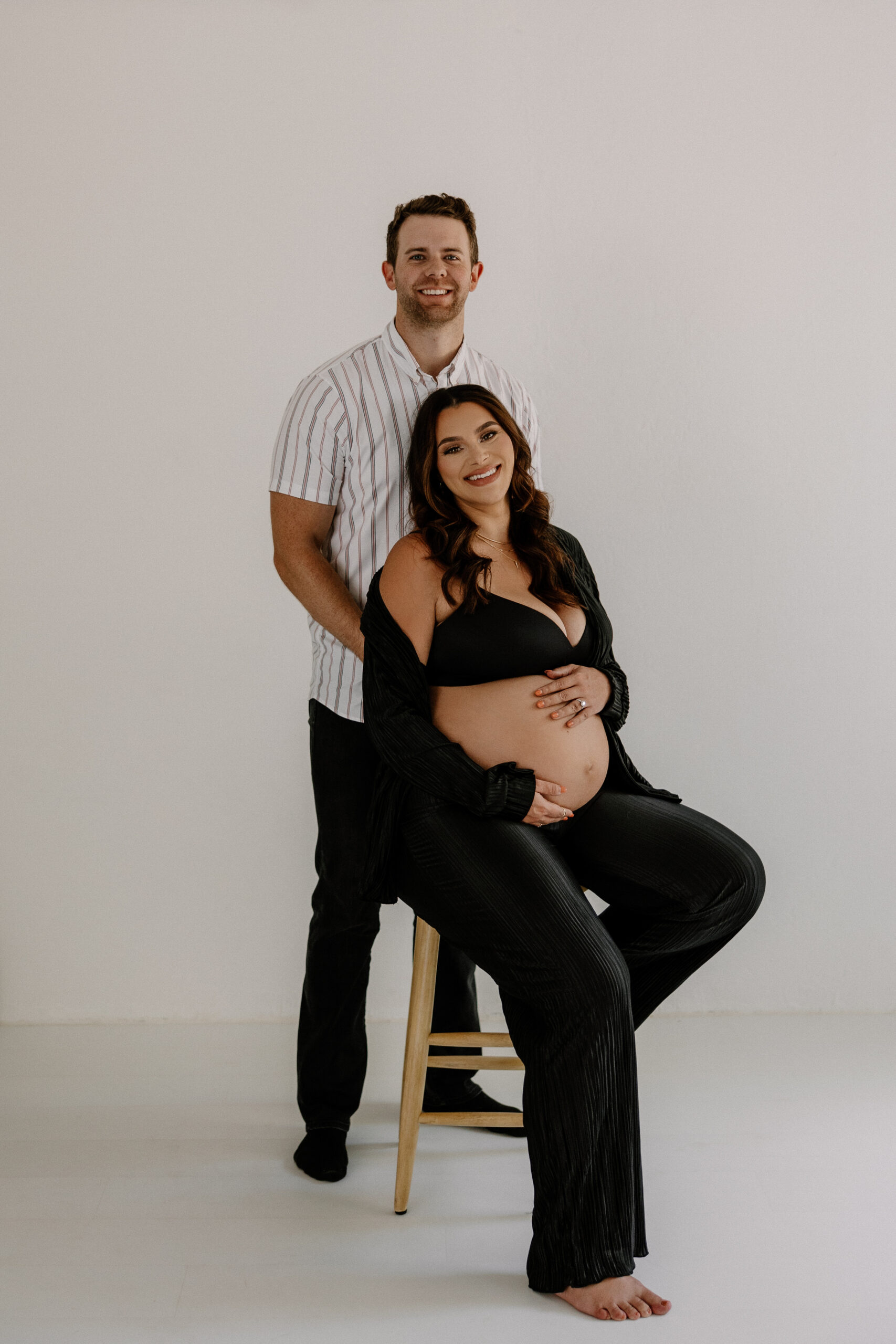 mom to be sitting on a stool and dad to be behind her smiling 