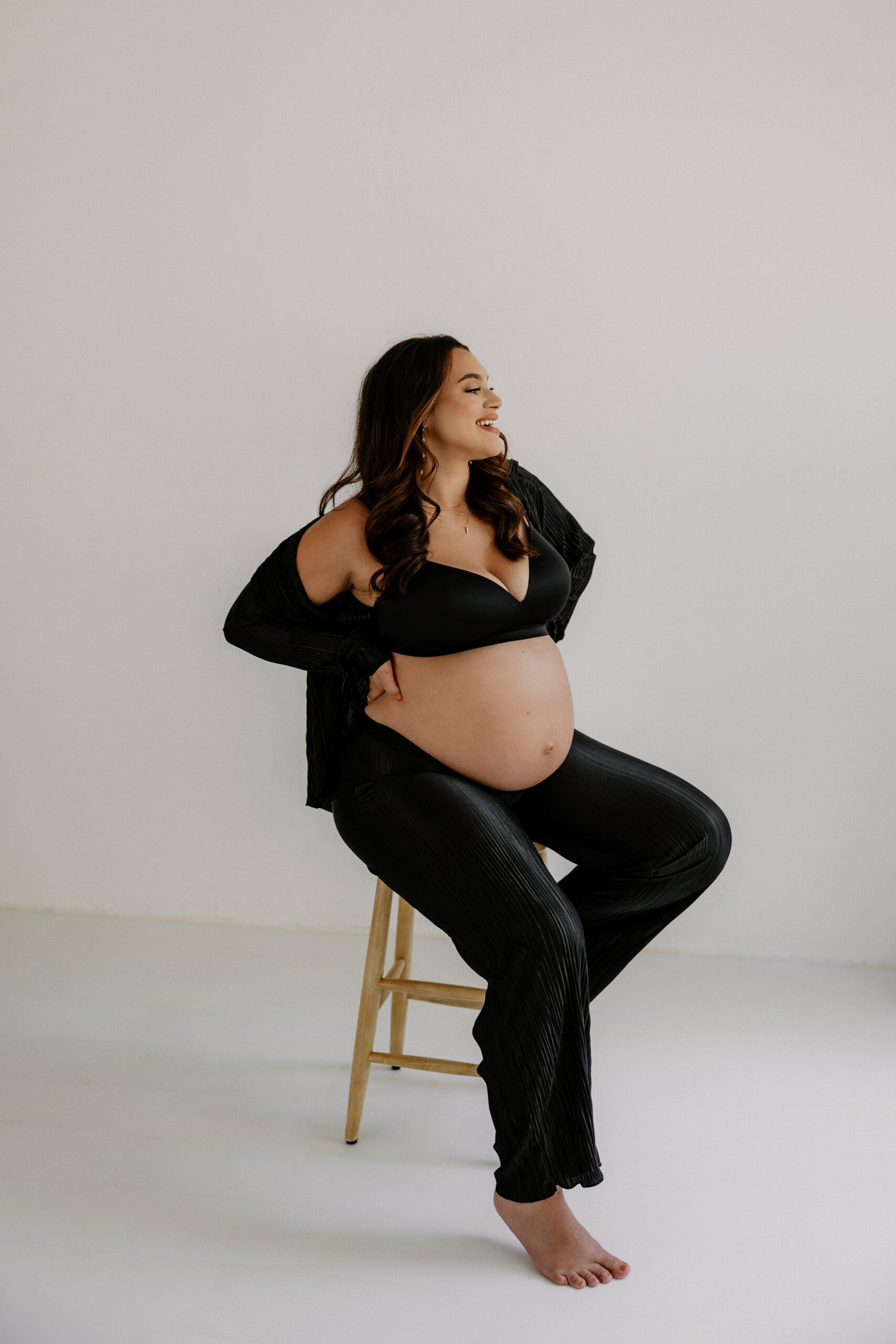 pregnant woman sitting on a stool and smiling during editorial maternity photoshoot 