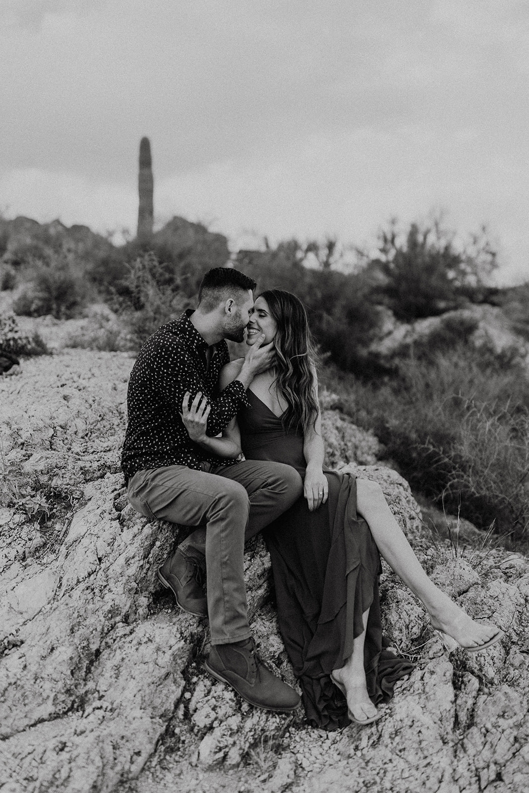 black and white of couple sitting on a rock about to kiss during canyon lake arizona engagement pictures