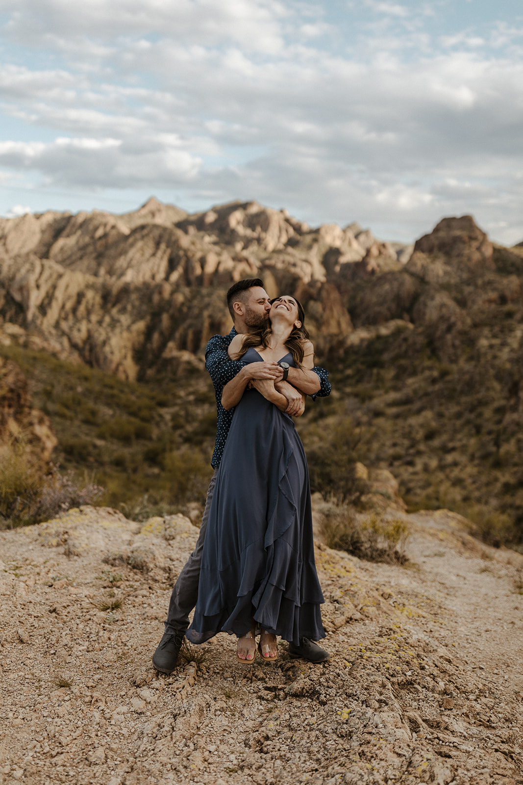 fiance hugging other fiance from behind in the mountains 