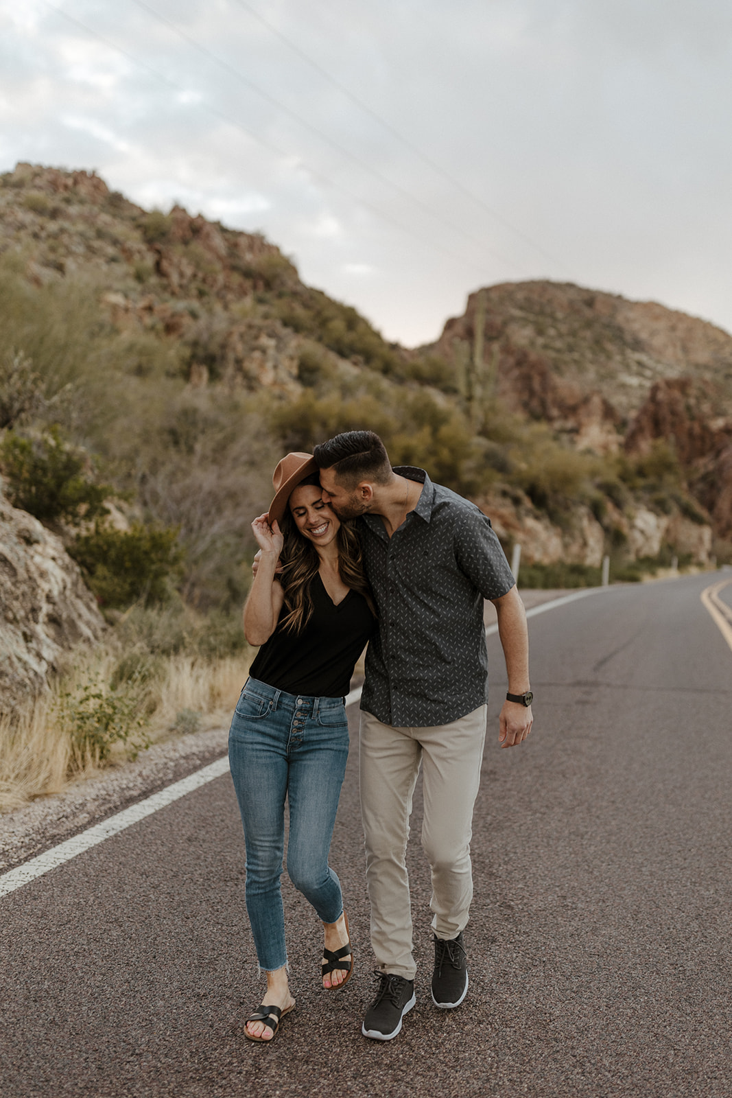couple walking on a road and one fiance kissing the other during canyon lake arizona engagement pictures