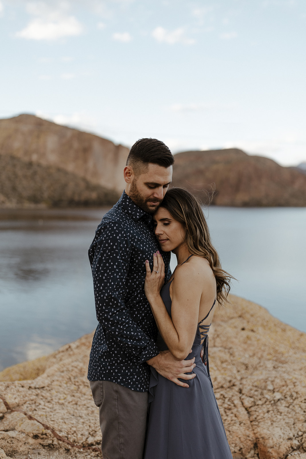 couple holding each other with their eyes closed with a lake behind them
