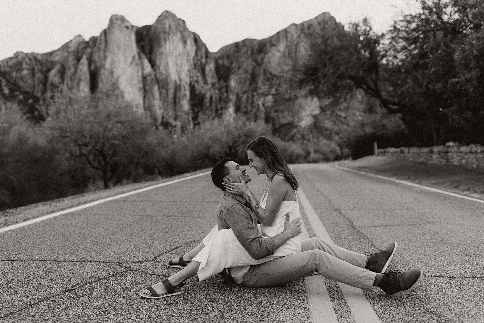 newly engaged couple sitting on the road smiling at each other during engagement session in arizona 