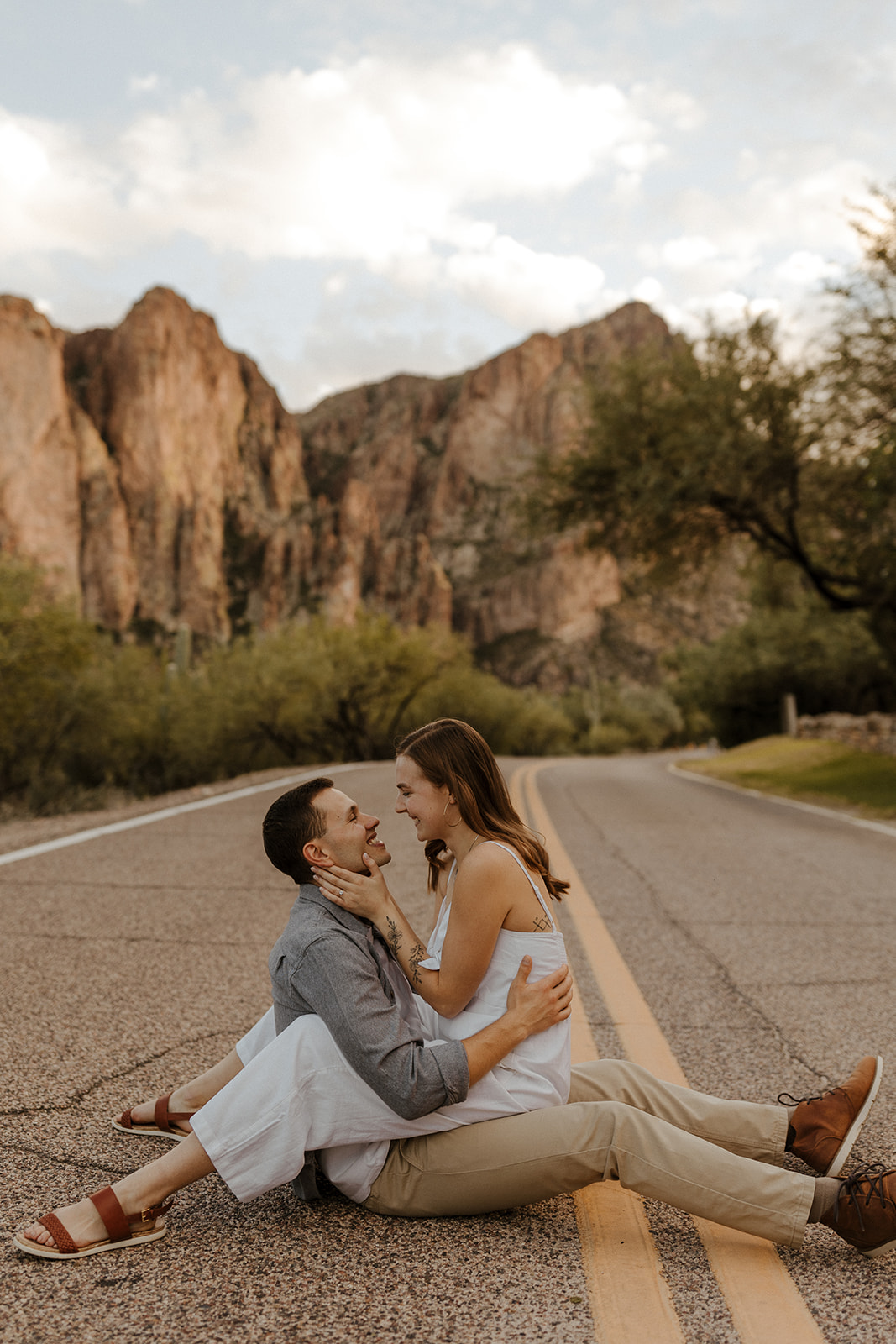 newly engaged couple sitting on each other on the road during engagement session in arizona 