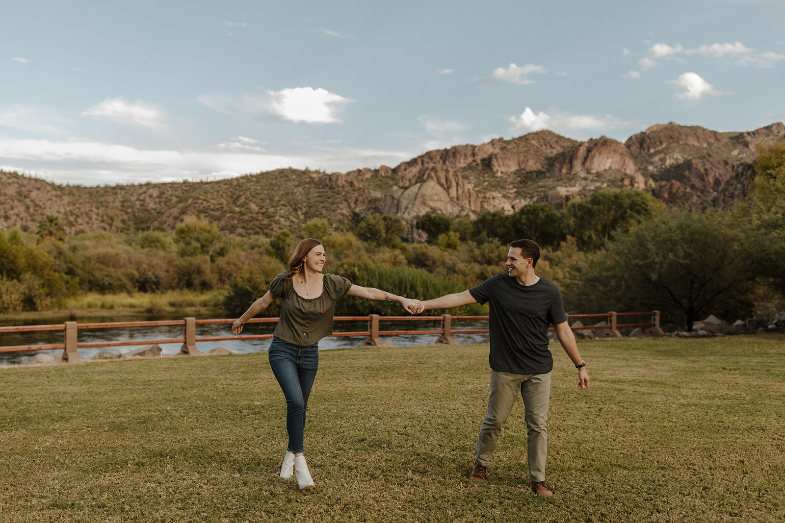 couple holding hands walking through the grass and smiling at each other at saguaro lake guest ranch Arizona 